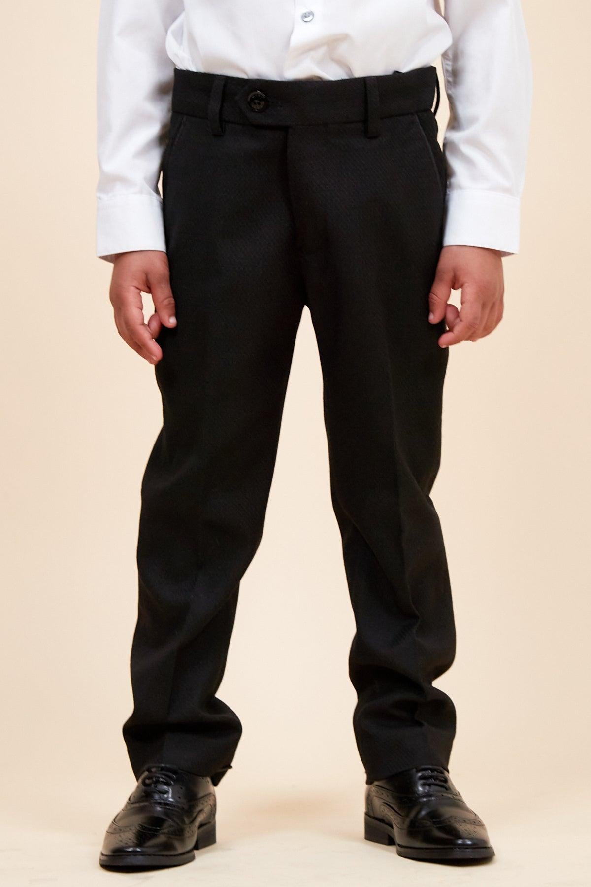 A child models the marcdarcy DALTON - Children's Black Tux Lapel Diamond Three Piece Suit, featuring a white shirt and black dress shoes, against a plain beige background. The child's face is not shown in the photo.