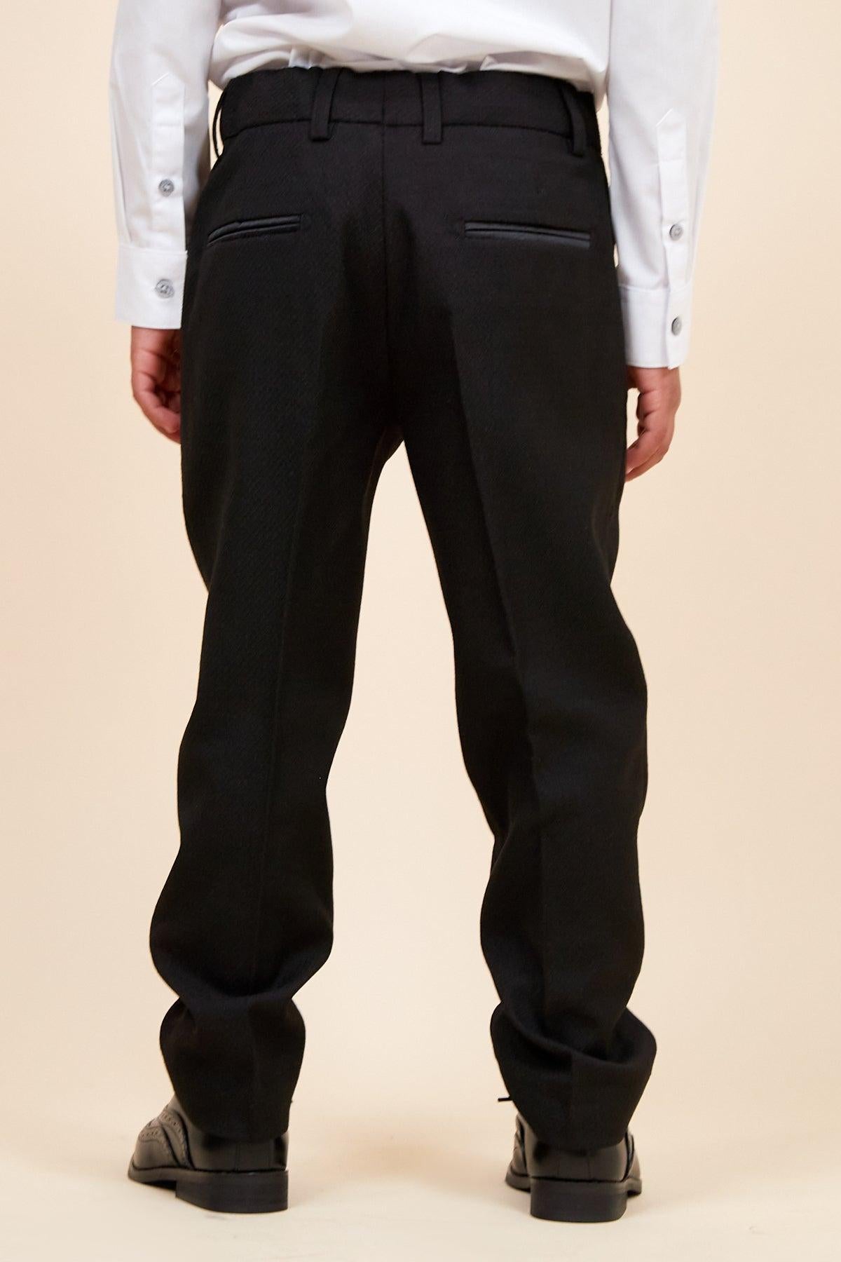 Back view of a boy in the marcdarcy DALTON Children's Black Tux Lapel Diamond Three Piece Suit, featuring a white dress shirt, black tuxedo pants with satin trim, and black dress shoes—ideal for any formal event.