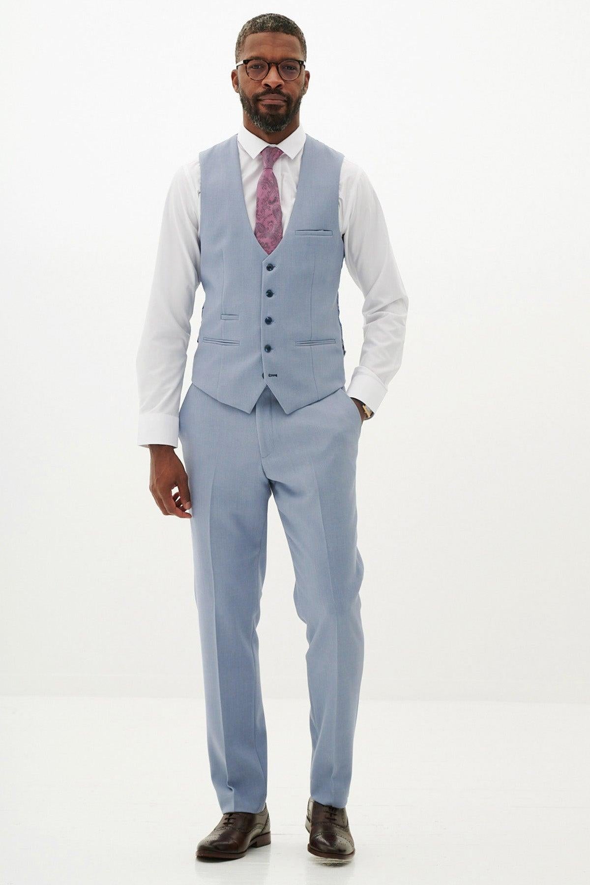 A Black man models the marcdarcy HM5 - Sky Blue Single Breasted Waistcoat, paired with a white shirt and pink patterned tie, standing with hands in his pockets against a white background.