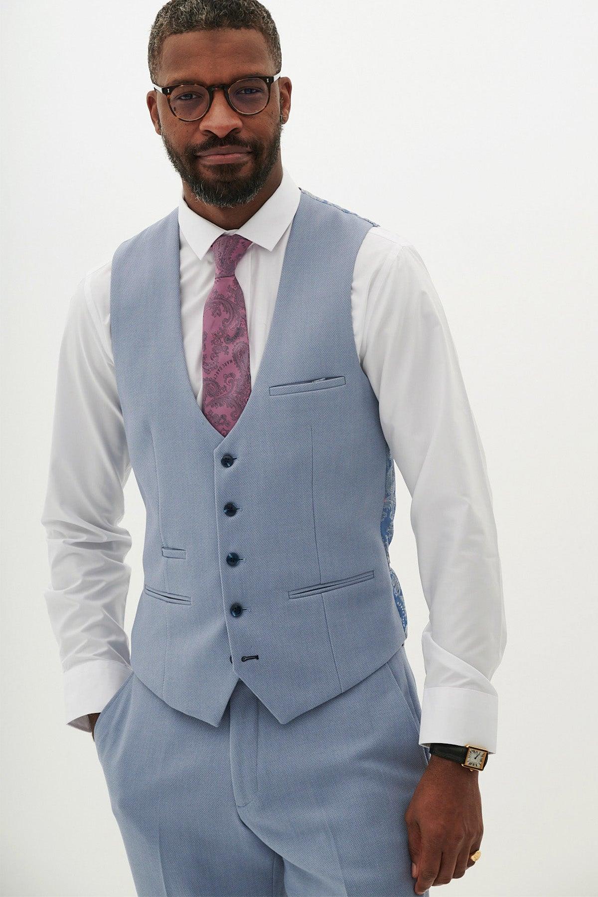 A man with glasses and a close beard models the marcdarcy HM5 - Sky Blue Single Breasted Waistcoat with matching trousers, white dress shirt, patterned purple tie, and wristwatch against a plain white background.