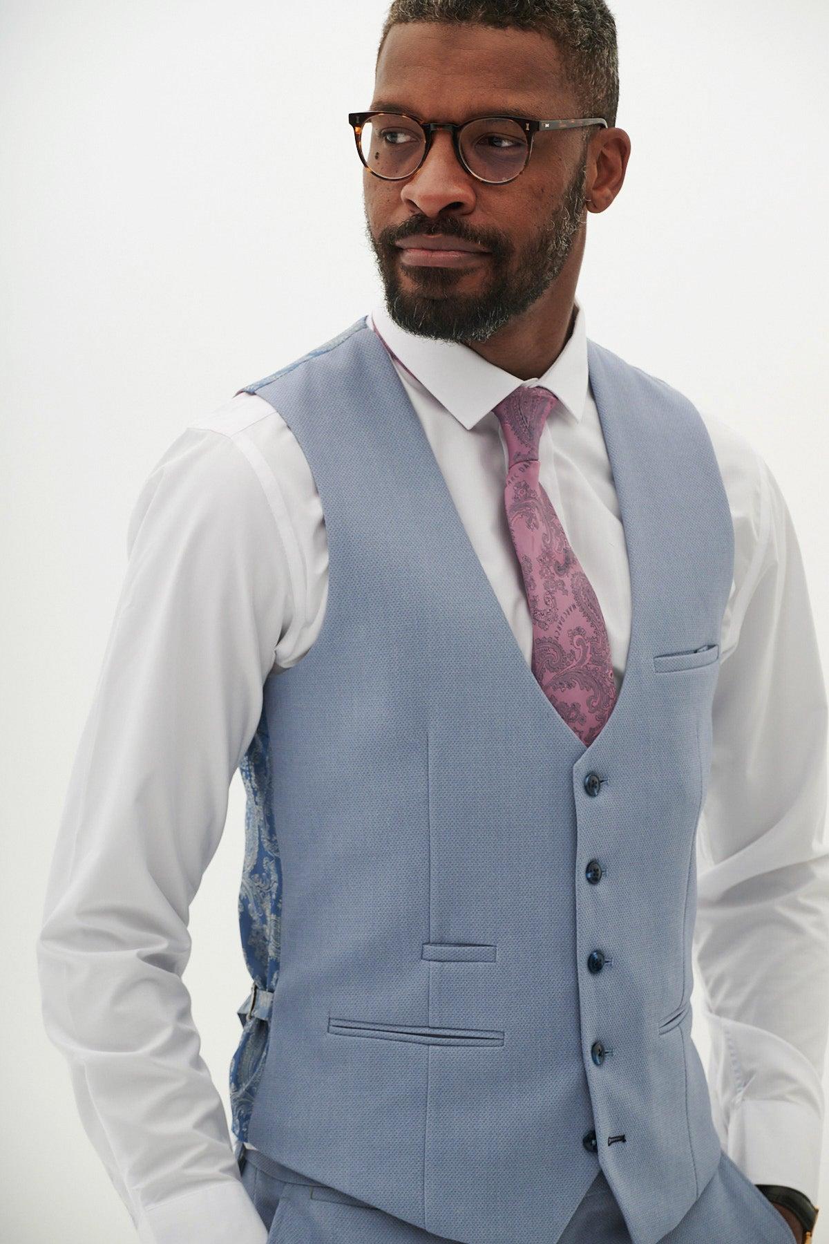 A Black man wearing glasses, a white shirt, and the marcdarcy HM5 Sky Blue Single Breasted Waistcoat with patterned lining, paired with a pink paisley tie.