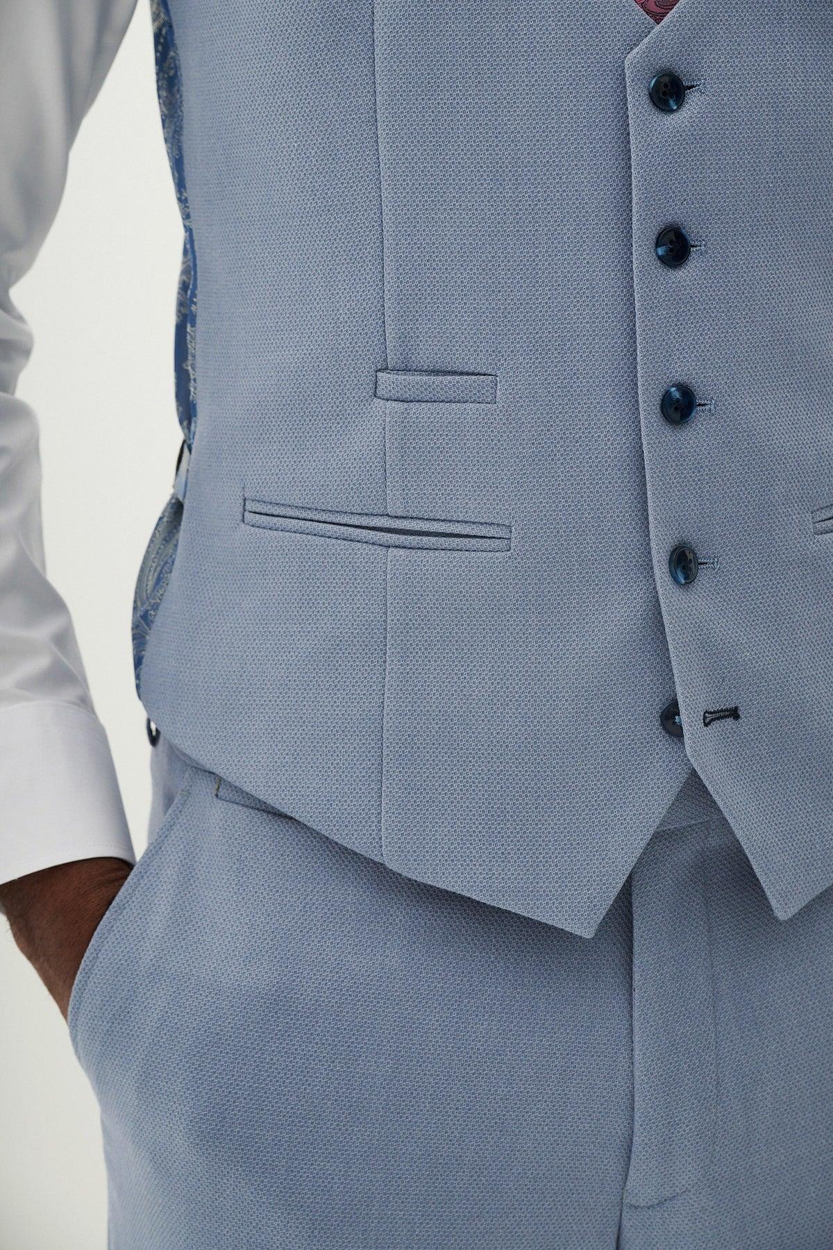 A person wears the marcdarcy HM5 Sky Blue Single Breasted Waistcoat and matching trousers over a white shirt. The slim fit waistcoat features dark buttons, subtle pockets, and one hand casually in the pocket for a polished finish.