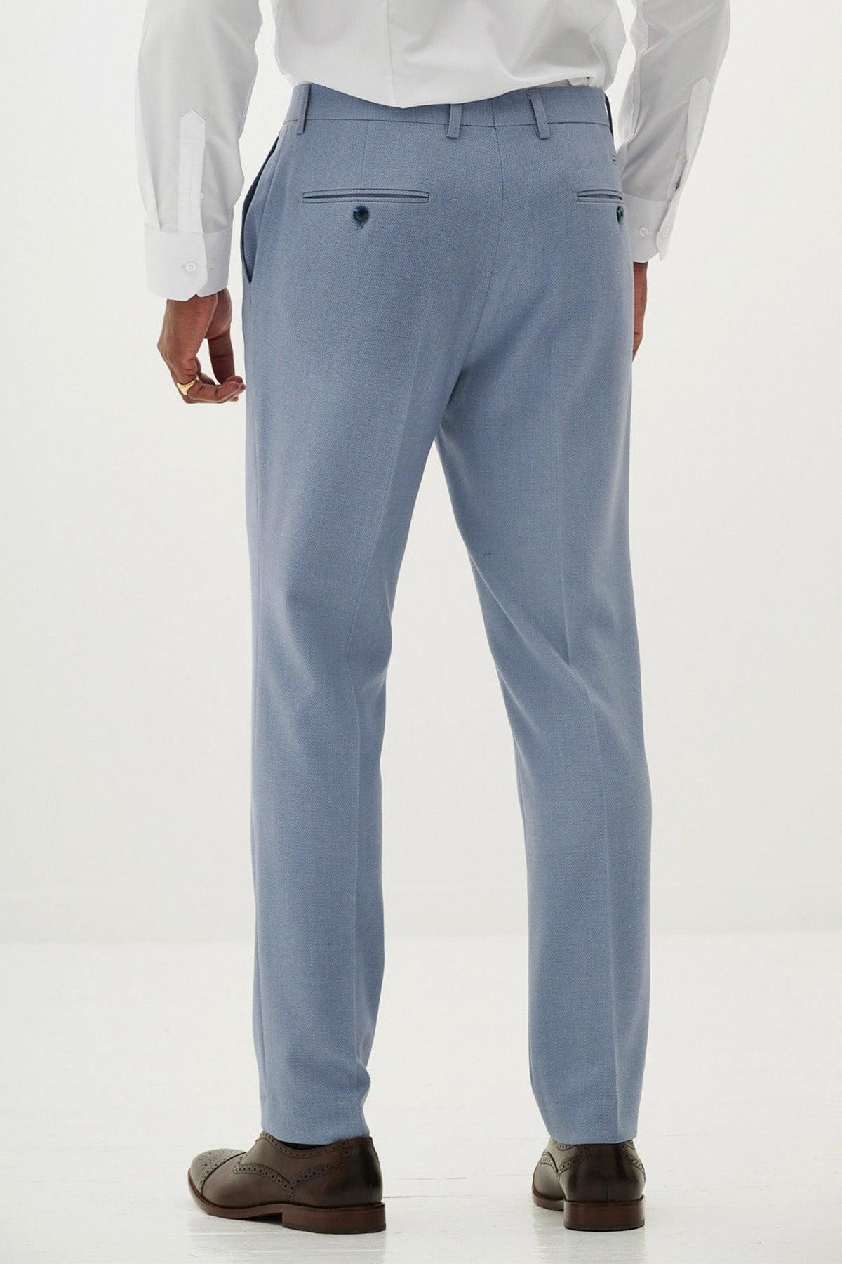 A man faces away, wearing the Marc Darcy HM5 - Sky Tailored Two Piece Suit and brown dress shoes. The suit pants have buttoned back pockets. He pairs them with a white dress shirt against a plain white background.