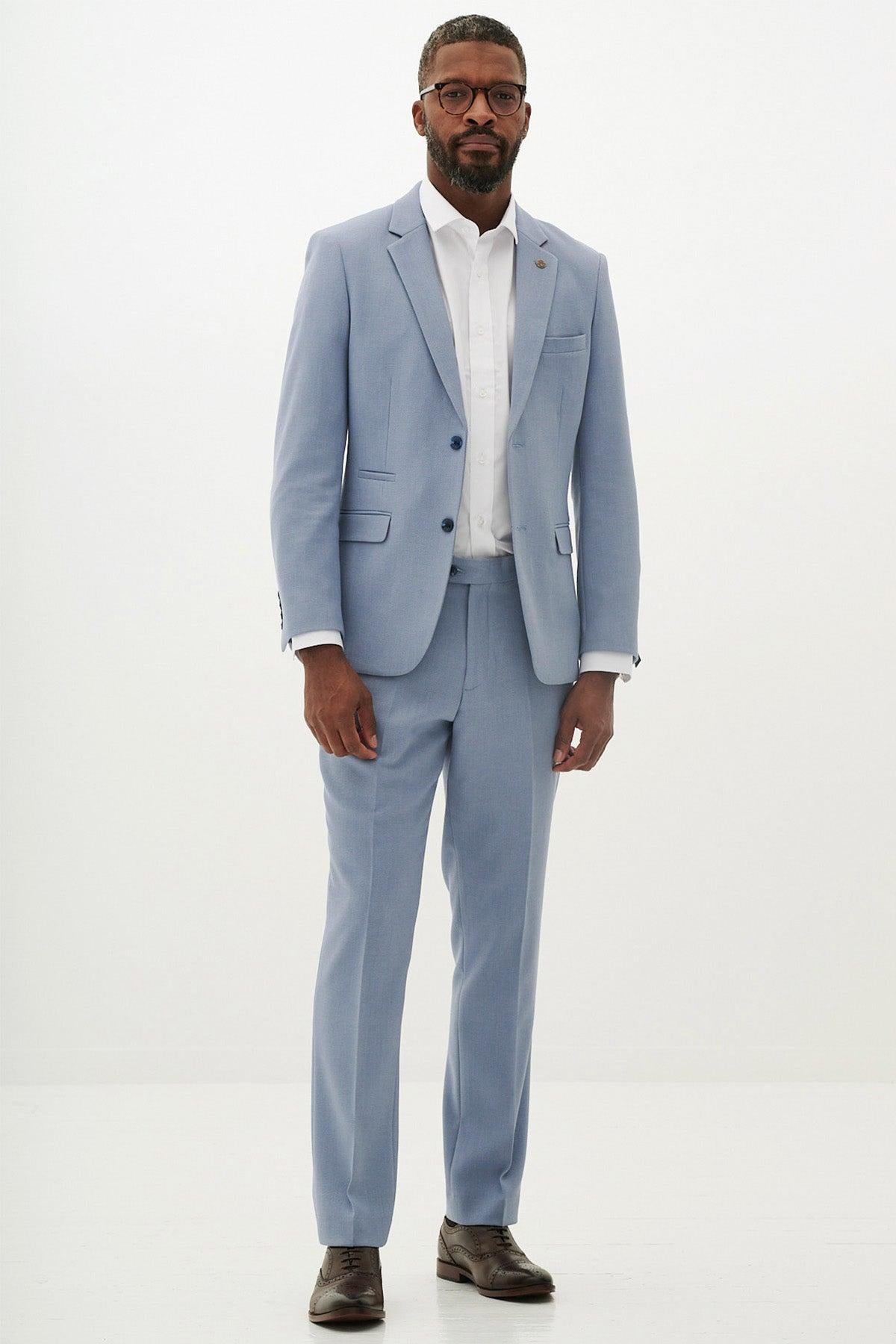 A man with short hair and a beard wears the marcdarcy HM5 - Sky Blue Tailored Blazer over a white shirt, paired with brown dress shoes and glasses, standing against a white background—ideal for special occasions.