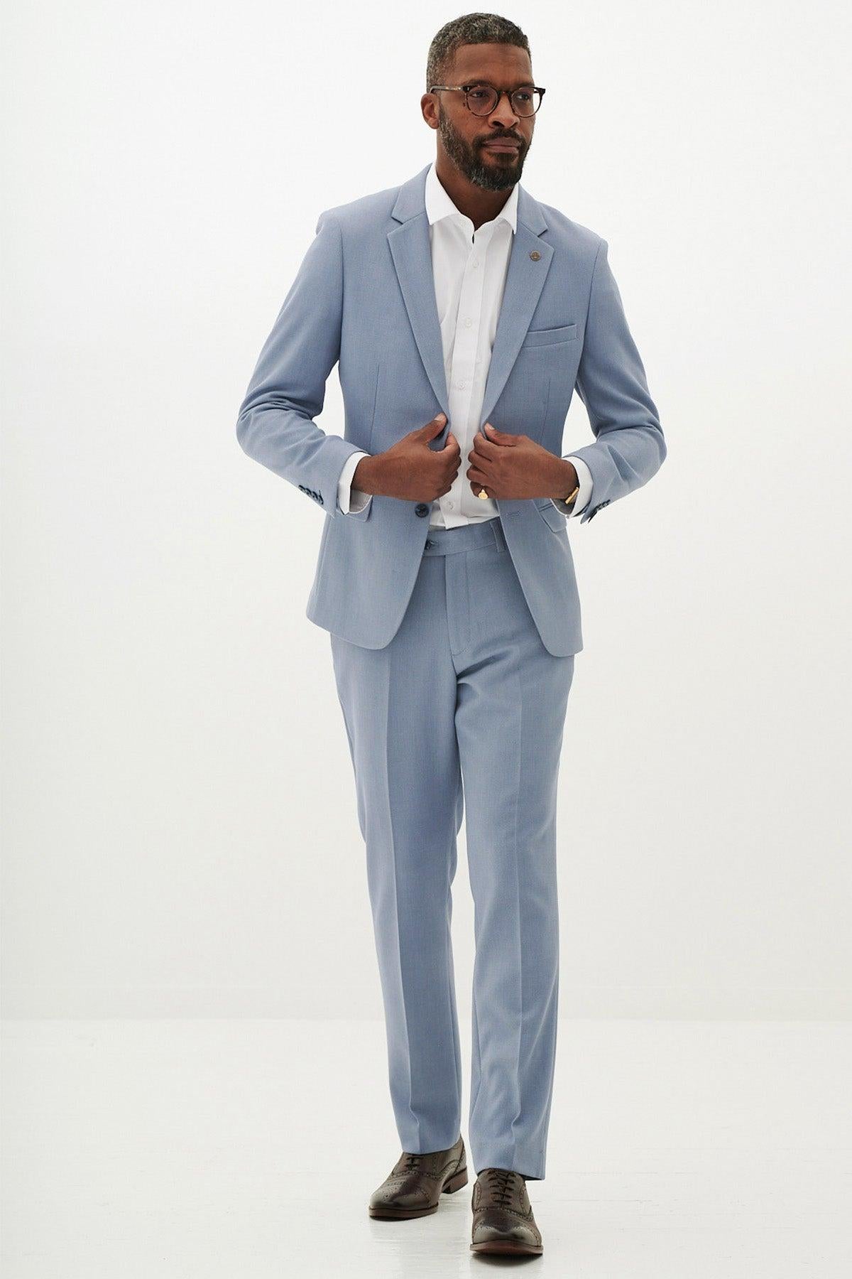 A Black man poses with his hands on his jacket while wearing the Marc Darcy HM5 - Sky Tailored Two Piece Suit, paired with a white shirt and brown dress shoes.