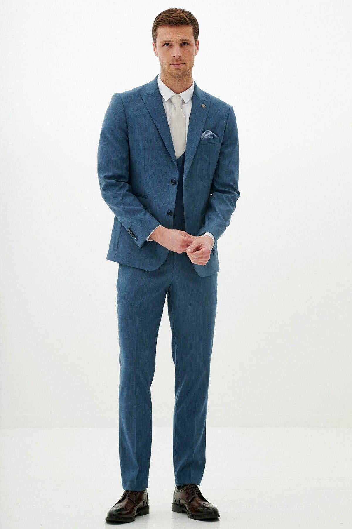 A man models the FINLEY - Teal Blue Three Piece Suit by Marc Darcy with a white shirt, light gray tie, pocket square, and dark brown dress shoes—perfect for summer weddings. He faces the camera against a plain background, hands clasped.