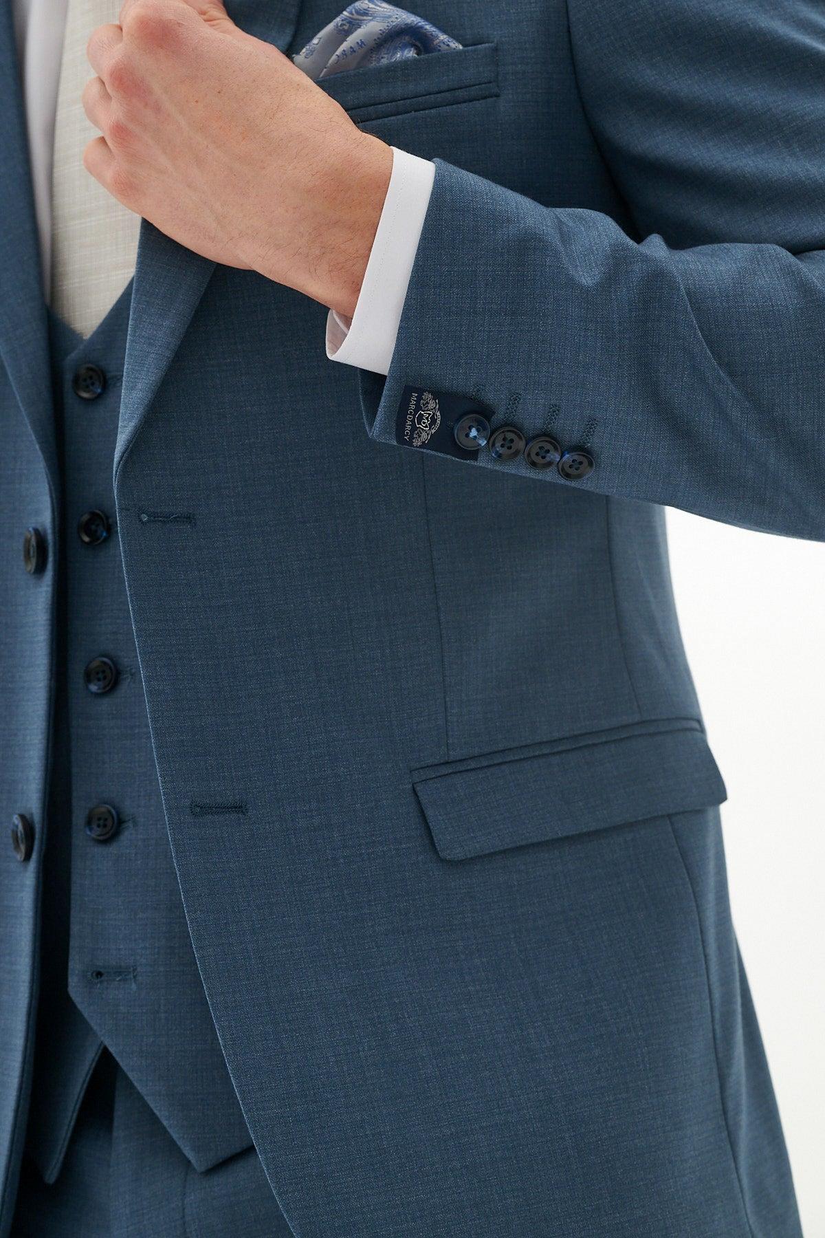 A person adjusts their jacket while wearing the Marc Darcy FINLEY Teal Blue Three Piece Suit with a matching waistcoat, white shirt, and pocket square. The image highlights the torso and arm, keeping the face out of frame.