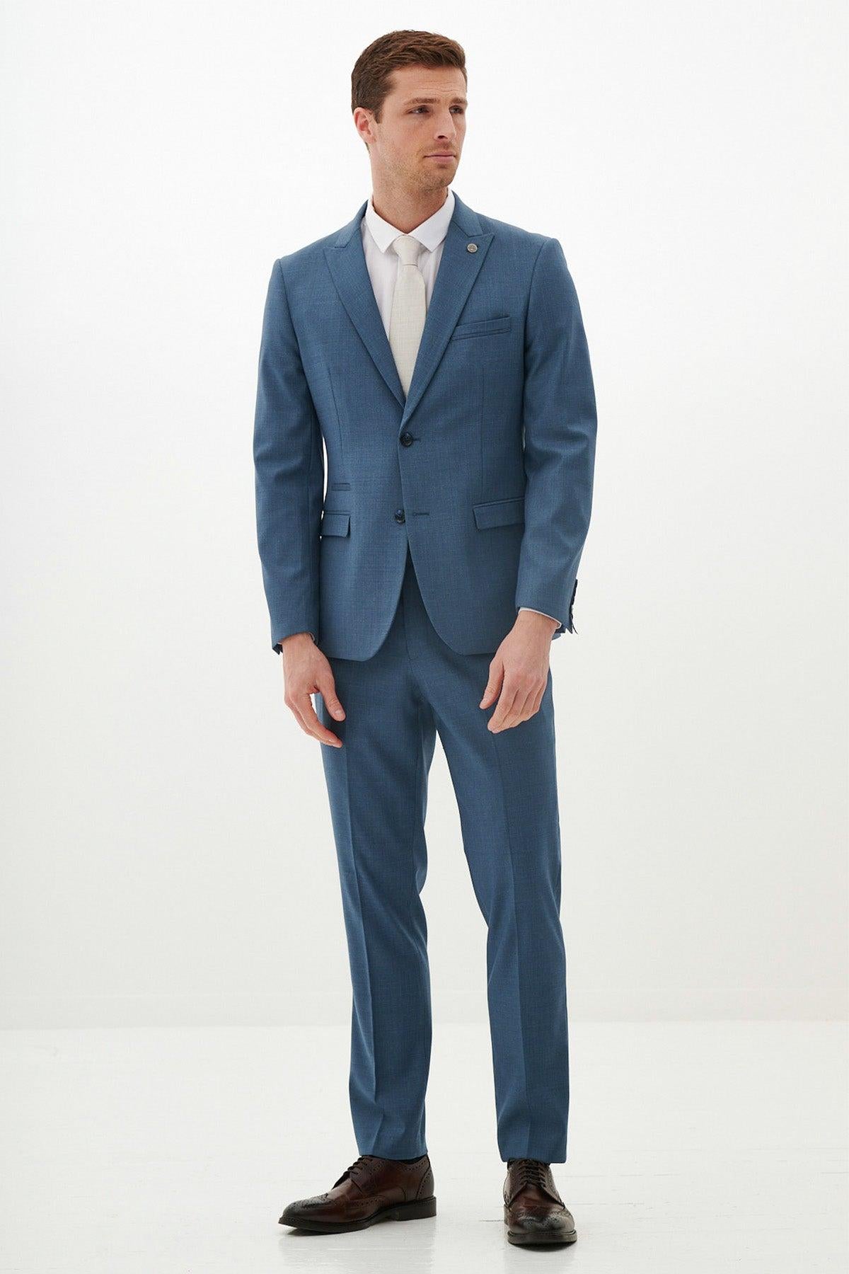 A man with short brown hair and a neutral expression stands against a white background, wearing the Marc Darcy FINLEY Teal Blue Two Piece Suit—ideal for summer weddings—with a white shirt, pale tie, and dark brown shoes.