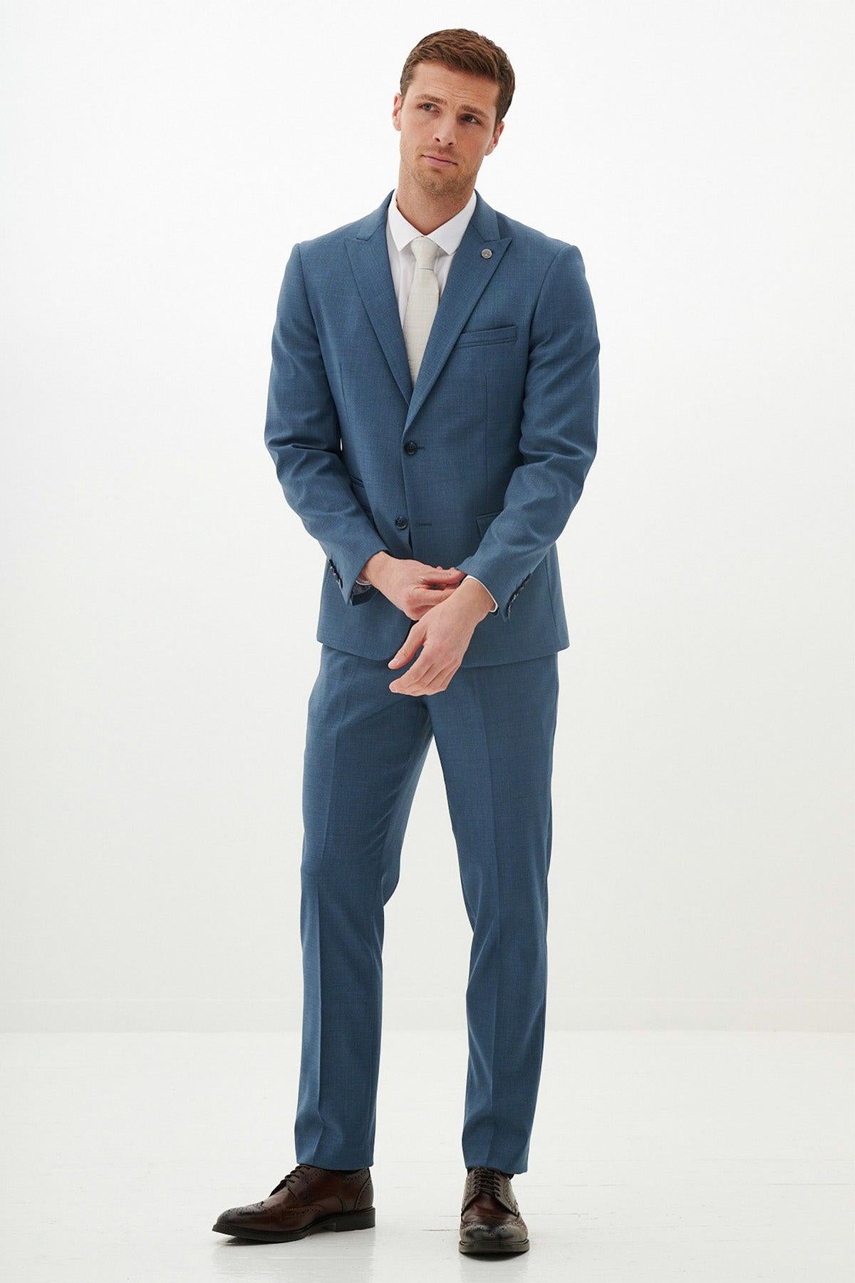 A man showcases the FINLEY - Teal Blue Two Piece Suit by Marc Darcy with a white shirt and cream tie—an ideal summer wedding look.