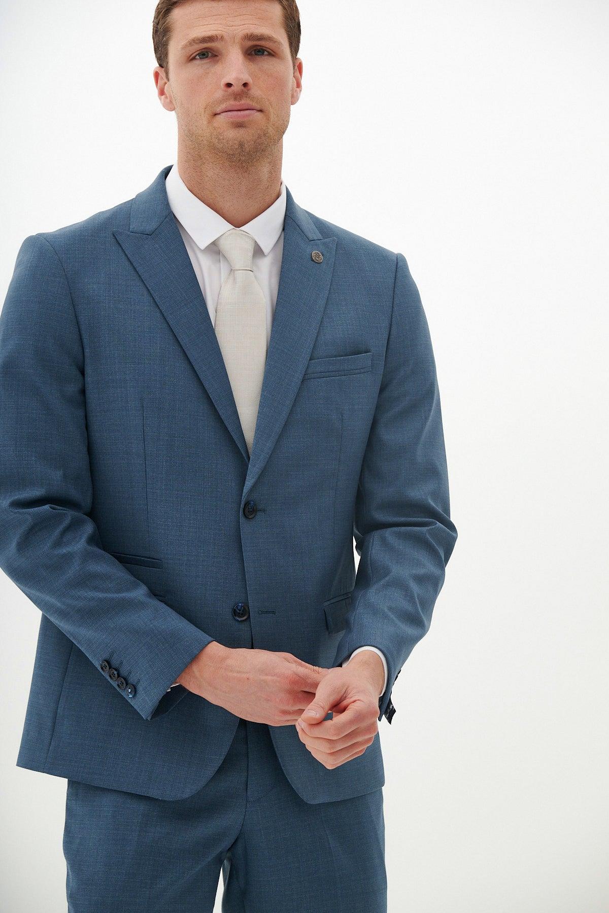 A man in the Marc Darcy FINLEY Teal Blue Tailored Blazer, white dress shirt, and white tie stands against a plain white background, looking forward while adjusting his blazer.