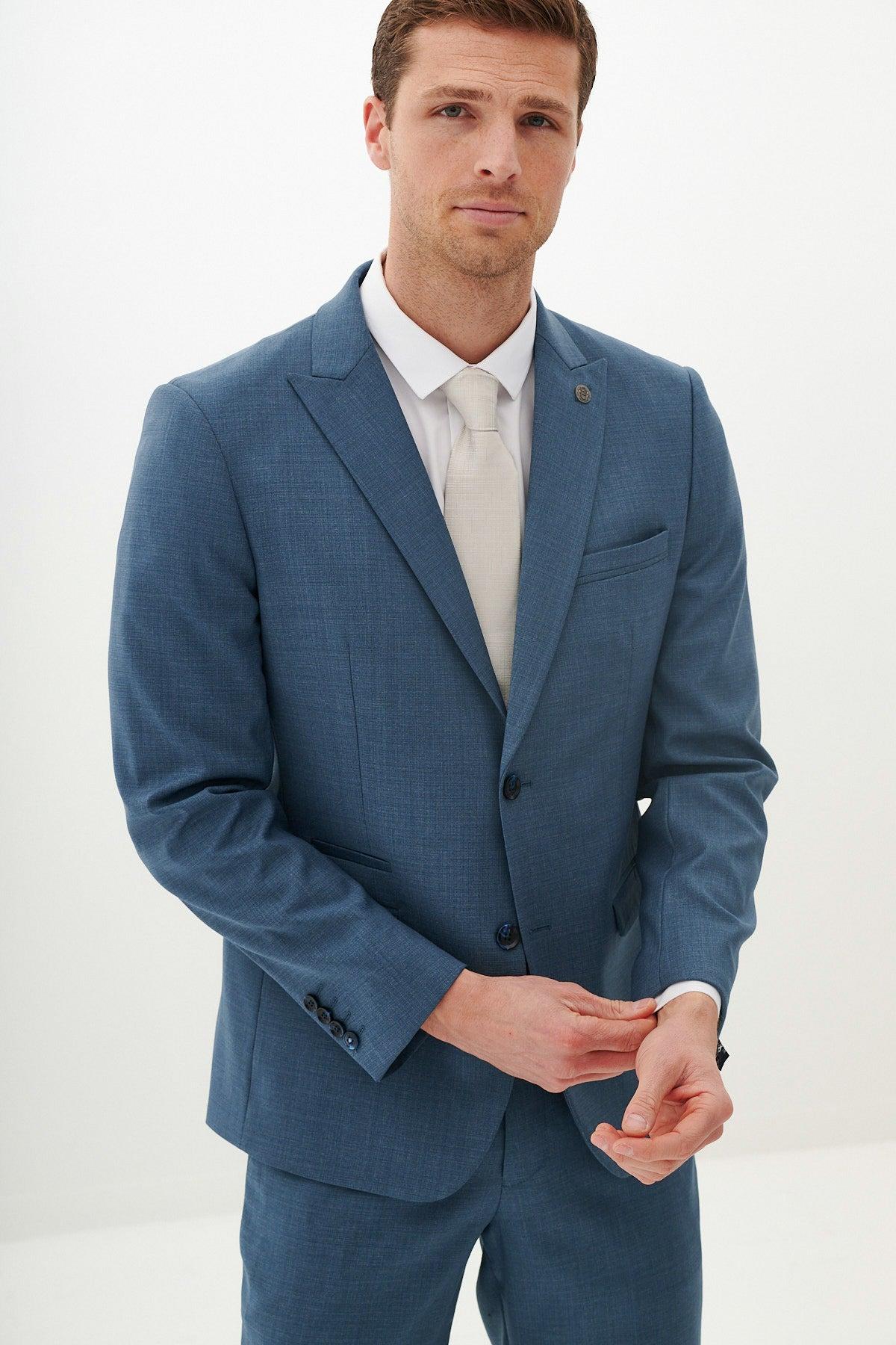 A man in a Marc Darcy FINLEY Teal Blue Tailored Blazer, white shirt, and light-colored tie adjusts his cuff.