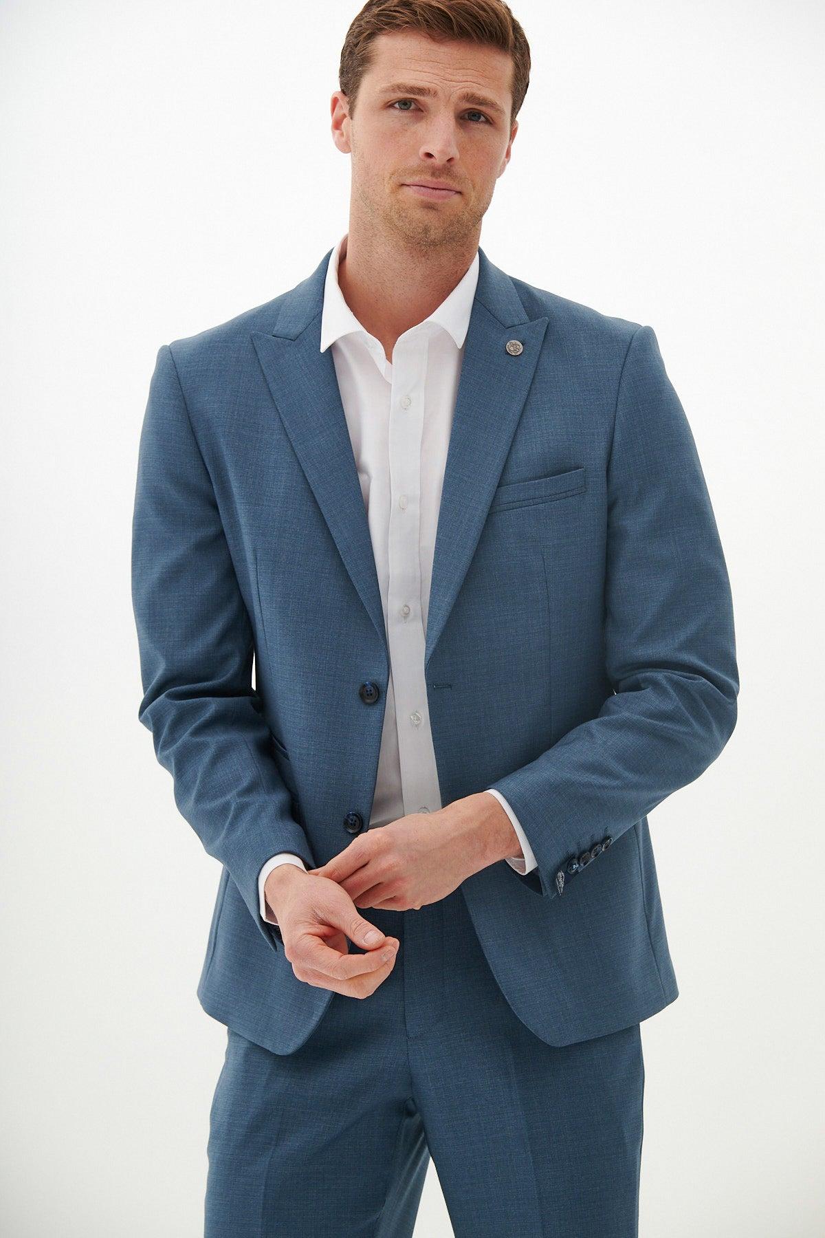A man wearing the Marc Darcy FINLEY - Teal Blue Tailored Blazer stands against a plain white background, looking at the camera with a neutral expression and adjusting his blazer sleeve.