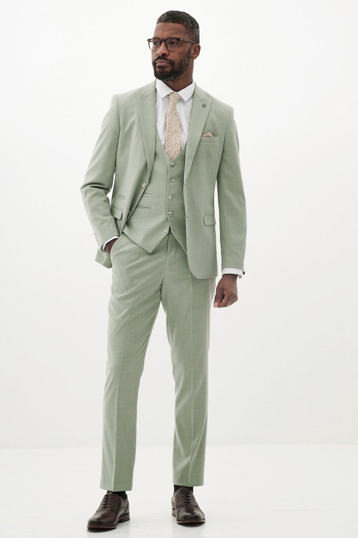 A man wears the Marc Darcy FINLEY Moss Green Three Piece Suit with a white shirt, patterned beige tie, and brown shoes against a plain white background—an ideal summer wedding outfit.