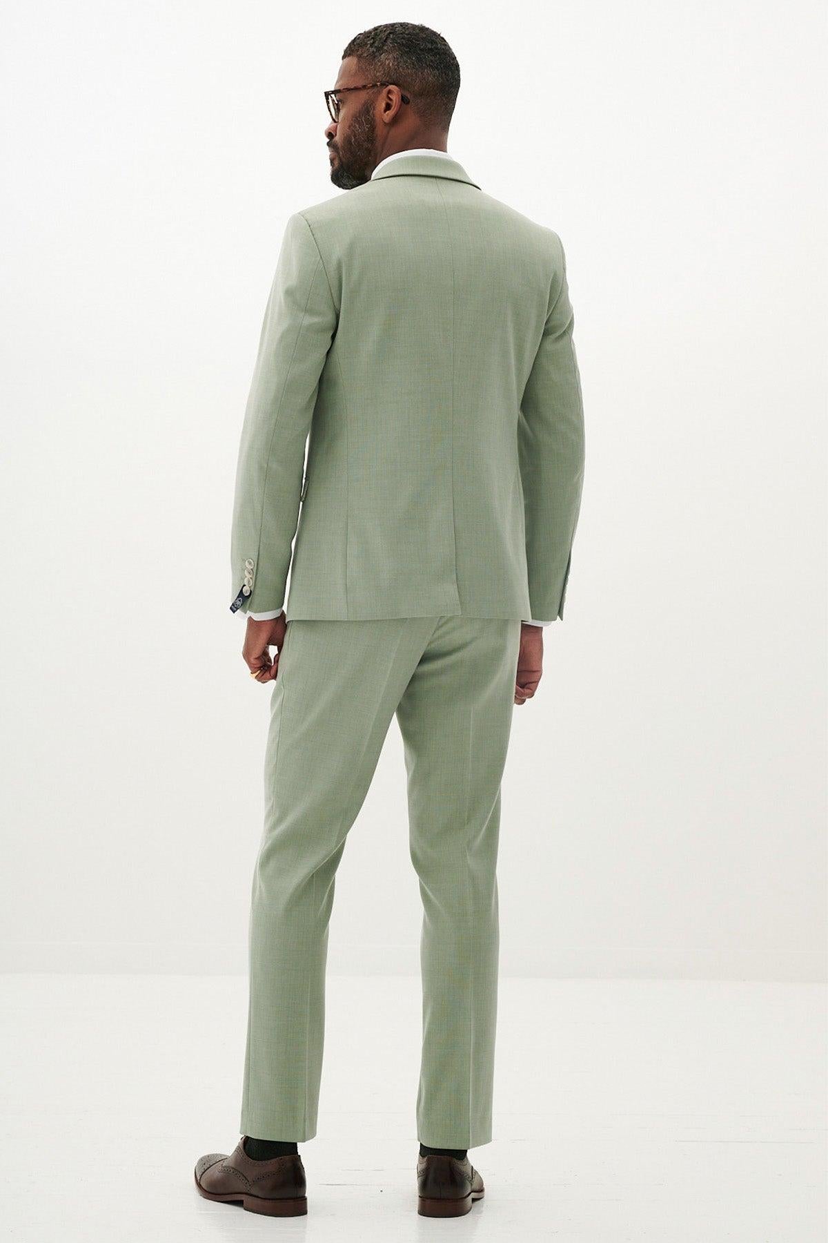 A man in the Marc Darcy FINLEY - Moss Green Two Piece Suit with a white shirt and brown dress shoes stands facing away, looking to the side against a plain white background.