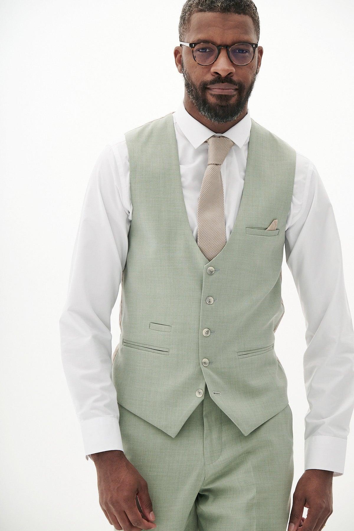 A man wearing glasses, the Marc Darcy FINLEY moss green single breasted waistcoat with matching trousers, a white shirt, beige tie, and pocket square stands against a plain white background—ideal summer formalwear.