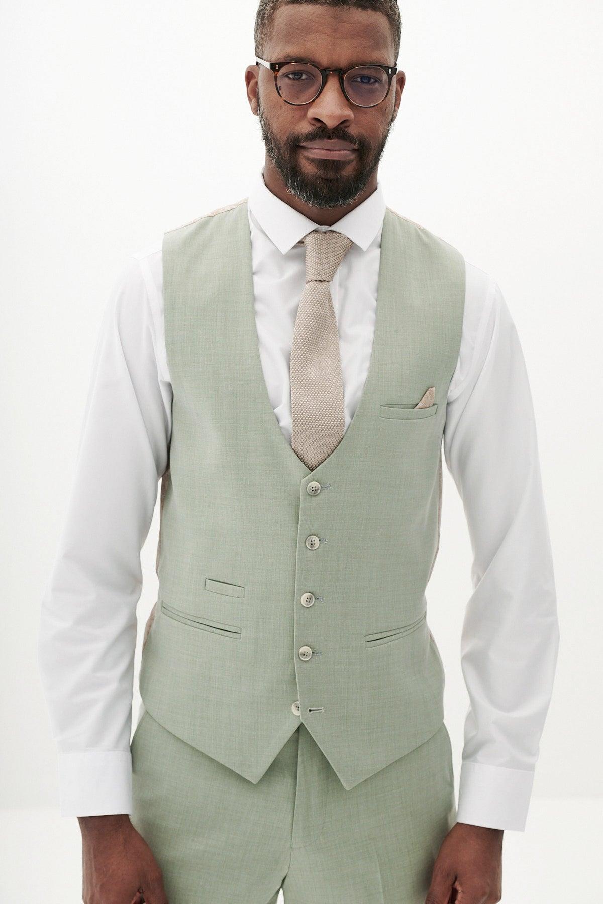 A Black man models the Marc Darcy FINLEY - Moss Green Three Piece Suit with a white shirt, tan tie, and glasses against a white background—the ideal choice for a stylish summer wedding look.