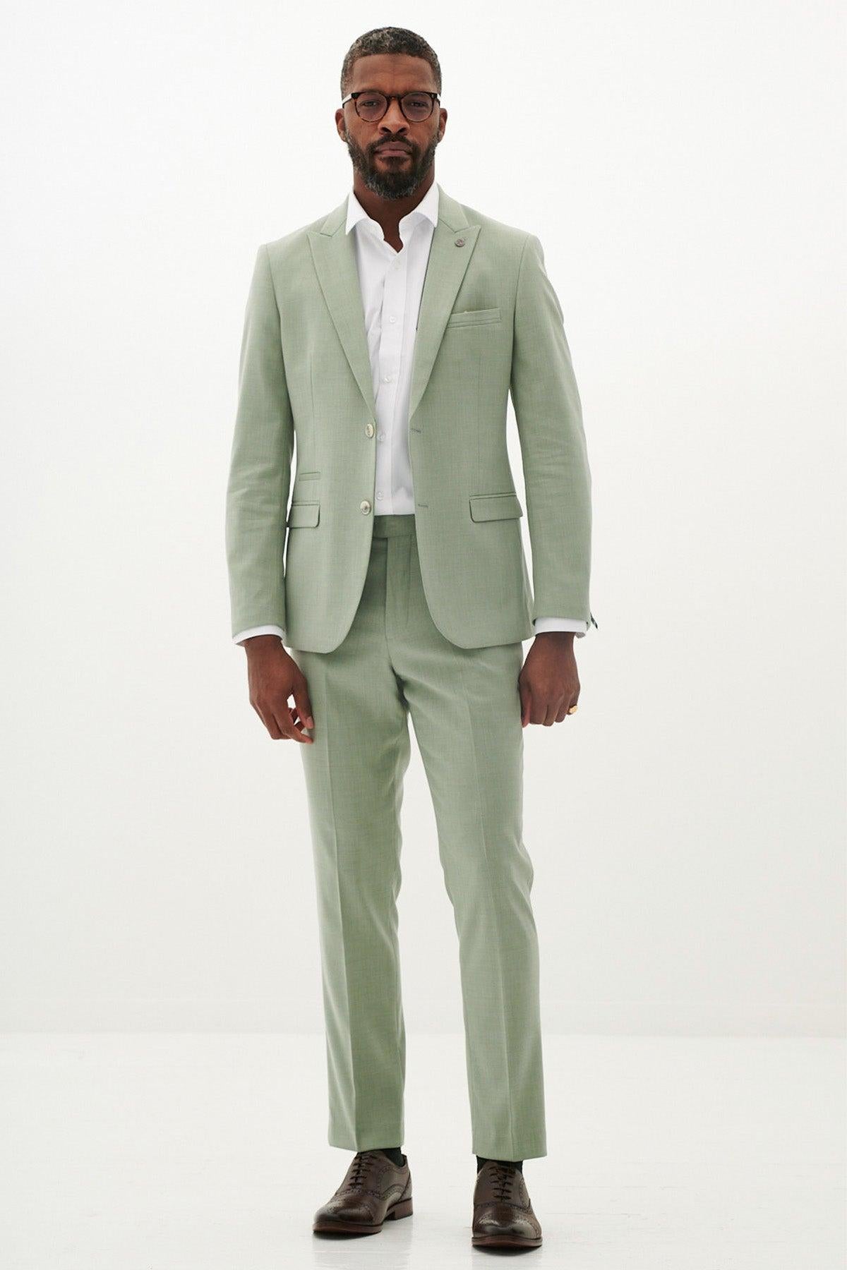 A Black man wearing glasses and a sage green suit stands against a white background, modeling the Marc Darcy FINLEY - Moss Green Two Piece Suit, perfect for summer weddings.