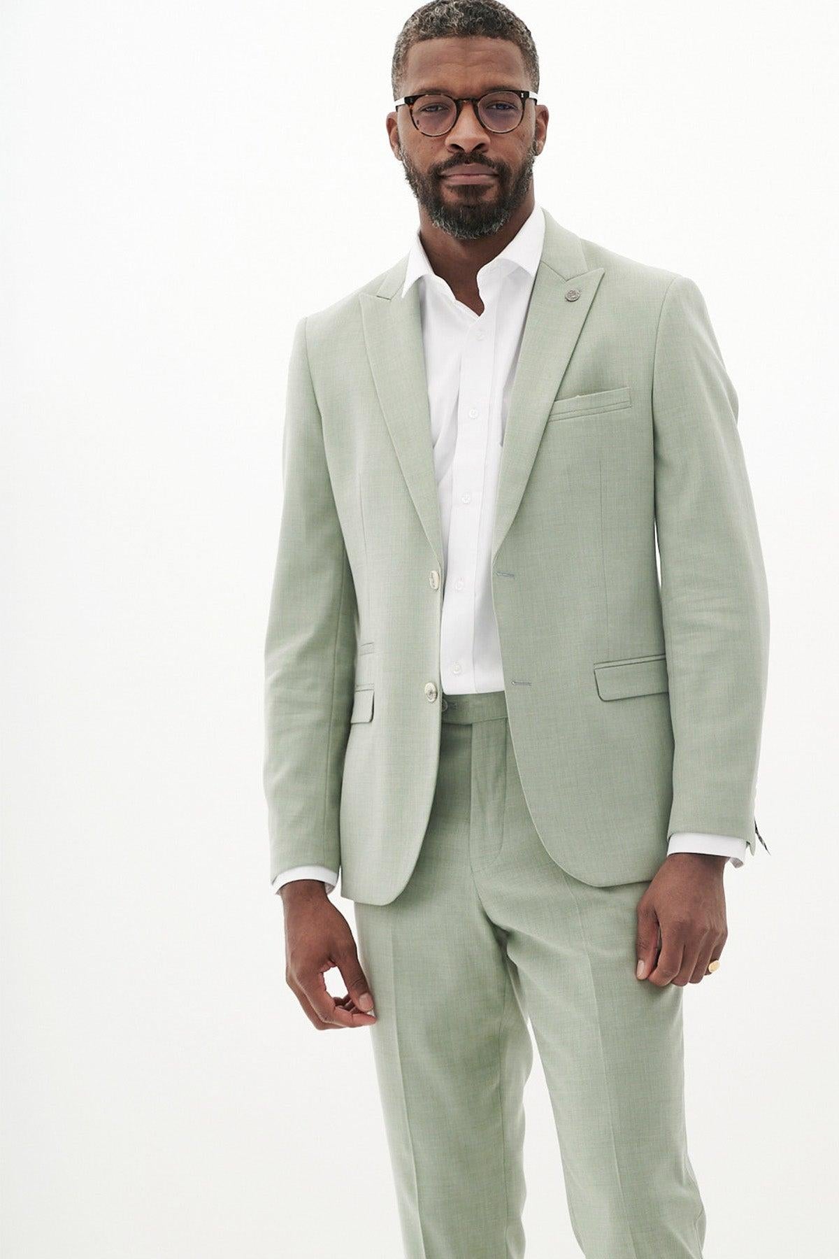 A man wearing glasses and a Marc Darcy FINLEY - Moss Green Tailored Blazer over a white dress shirt stands against a plain white background, looking confidently at the camera.
