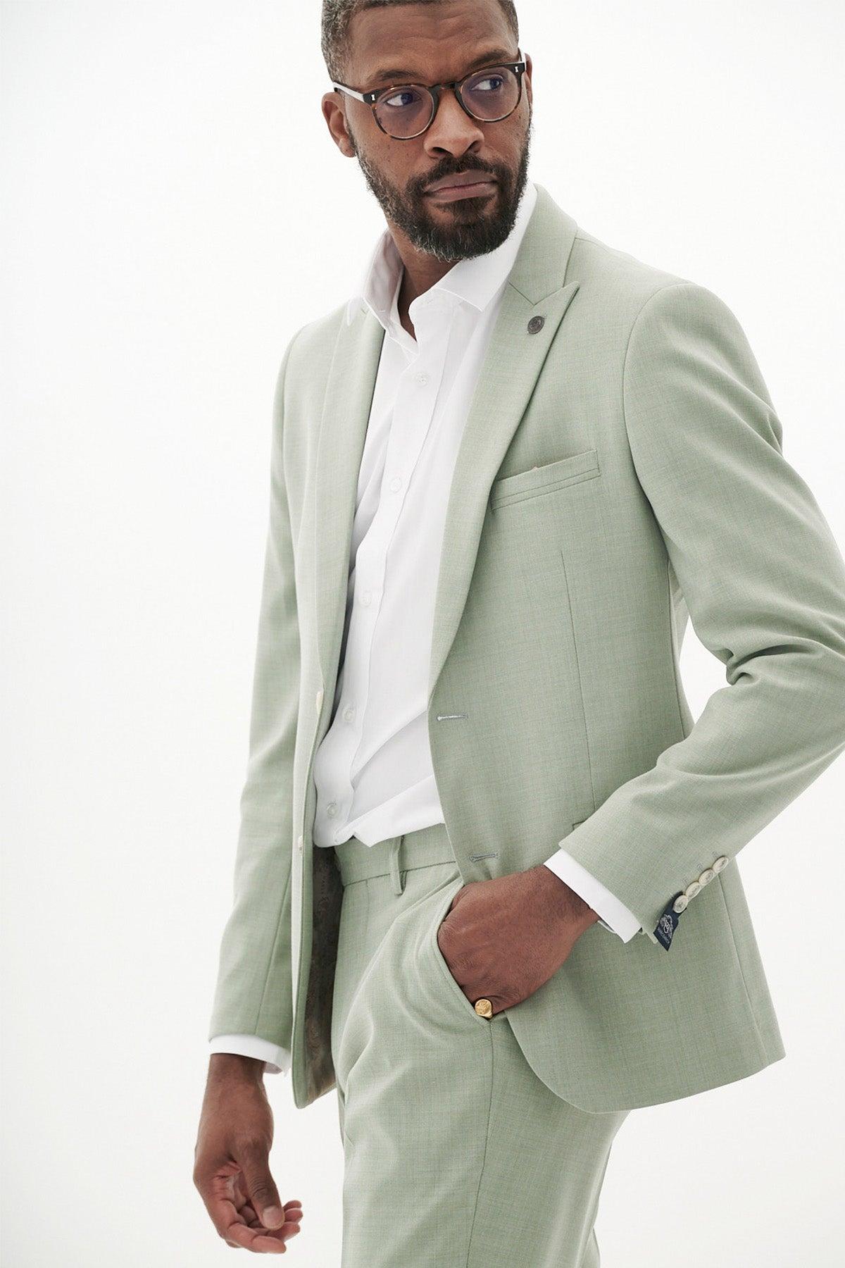A man in the Marc Darcy FINLEY - Moss Green Tailored Blazer over a white shirt, with glasses and a beard, his hand in his pocket—a casual yet polished spring-summer look.