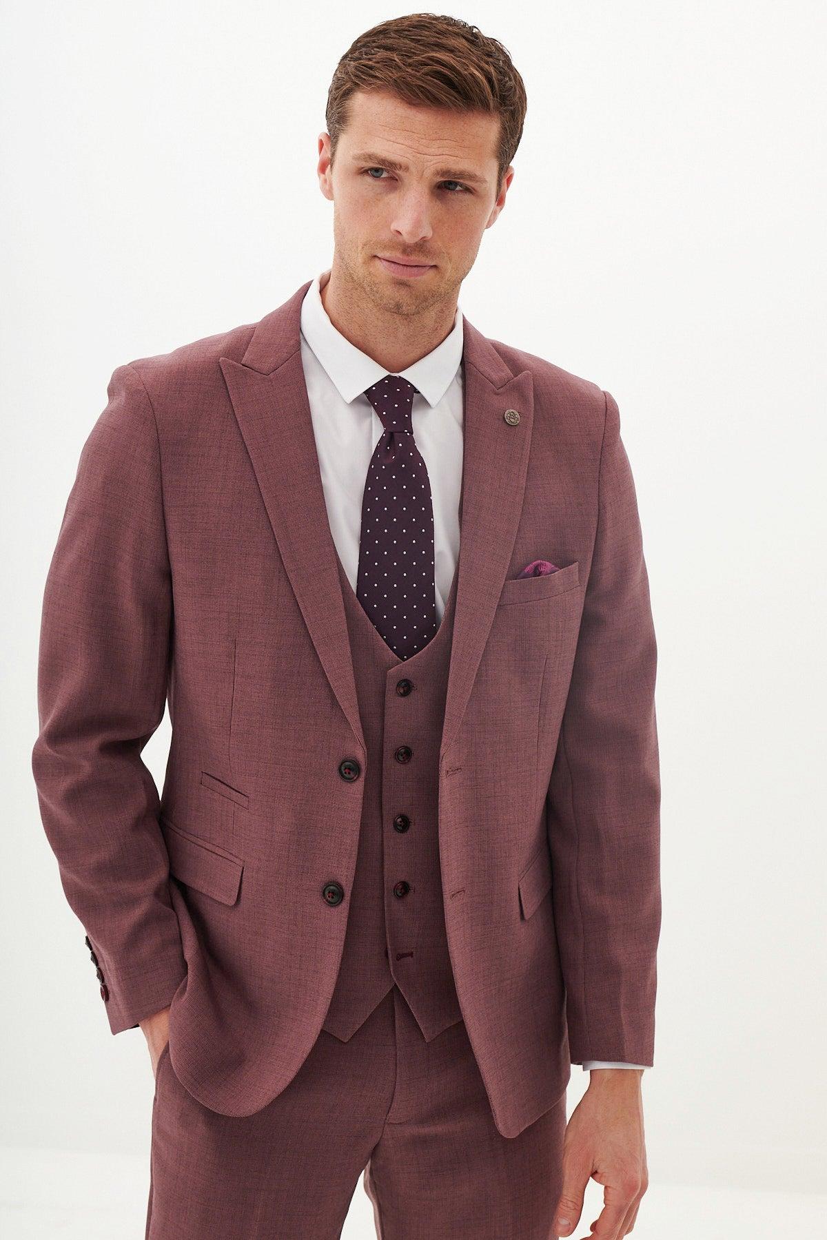 A man models the Marc Darcy MONTY - Mauve Three Piece Suit, paired with a white shirt and dark purple polka dot tie, posing with one hand in his pocket—perfect for summer weddings.