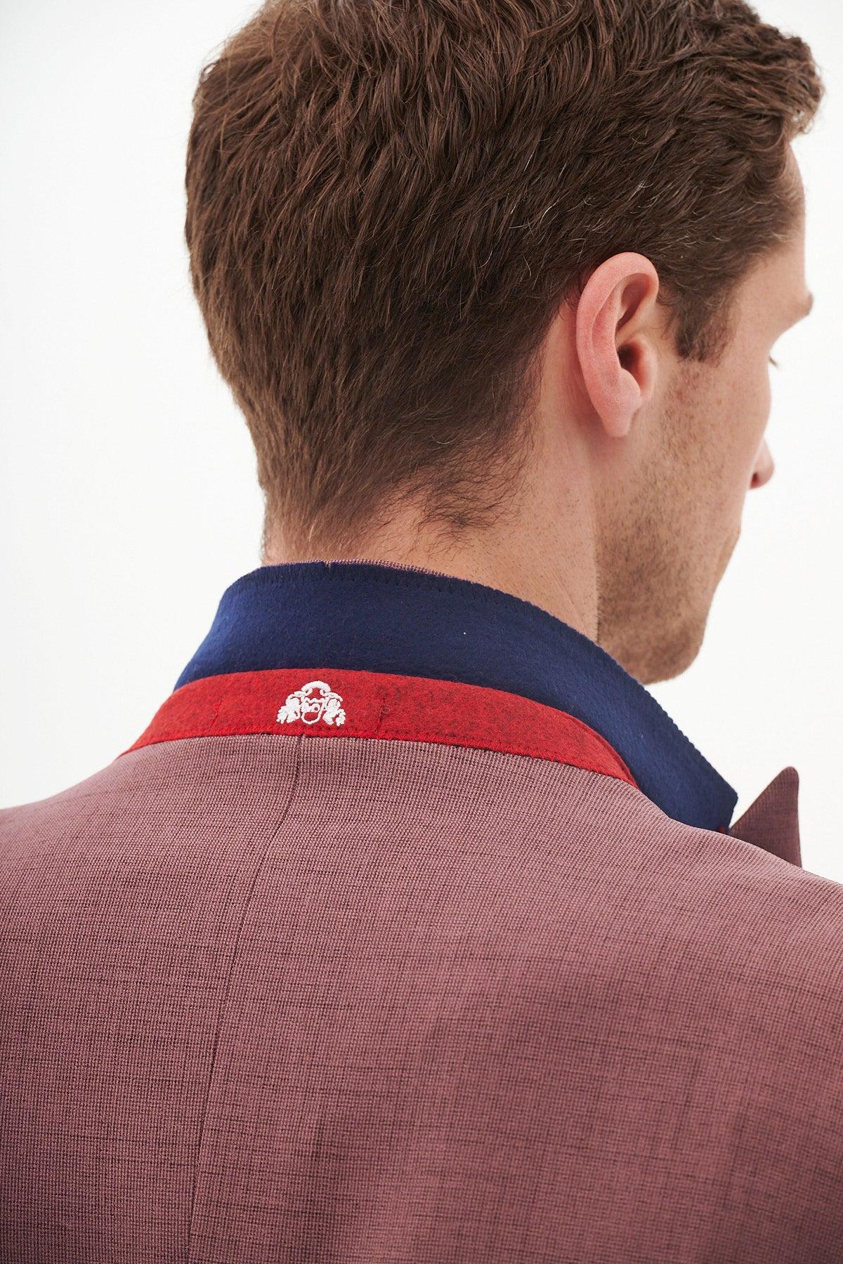 A man, seen from behind, wears the Marc Darcy MONTY - Mauve Tailored Blazer—a slim fit jacket with a textured finish, raised collar revealing blue underside with red trim, and white embroidered detail at the back—ideal for formalwear.