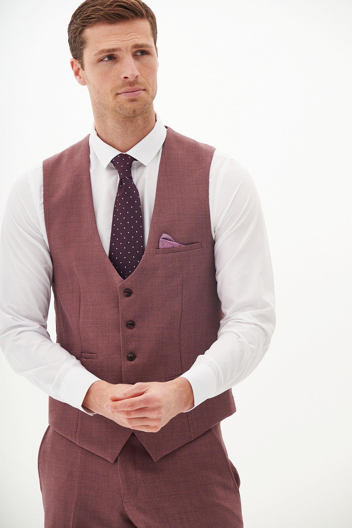 A man in a Marc Darcy BROMLEY Navy With Monty Waistcoat Suit, white shirt, and purple polka-dot tie, with his hands clasped in front of him.