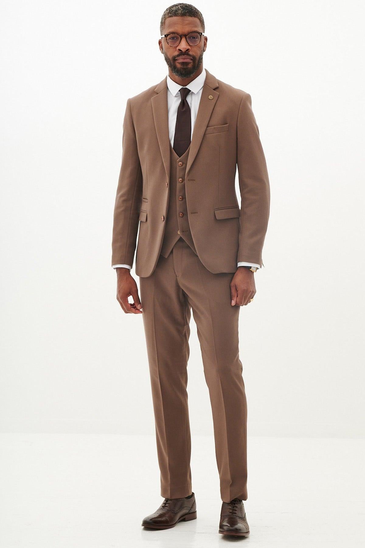A Black man wears the Marc Darcy West Bromwich Albion F.C. Collection HM5 Tan Tailored Suit, as seen on Michael Johnston, with a white shirt and brown tie, standing against a white background.
