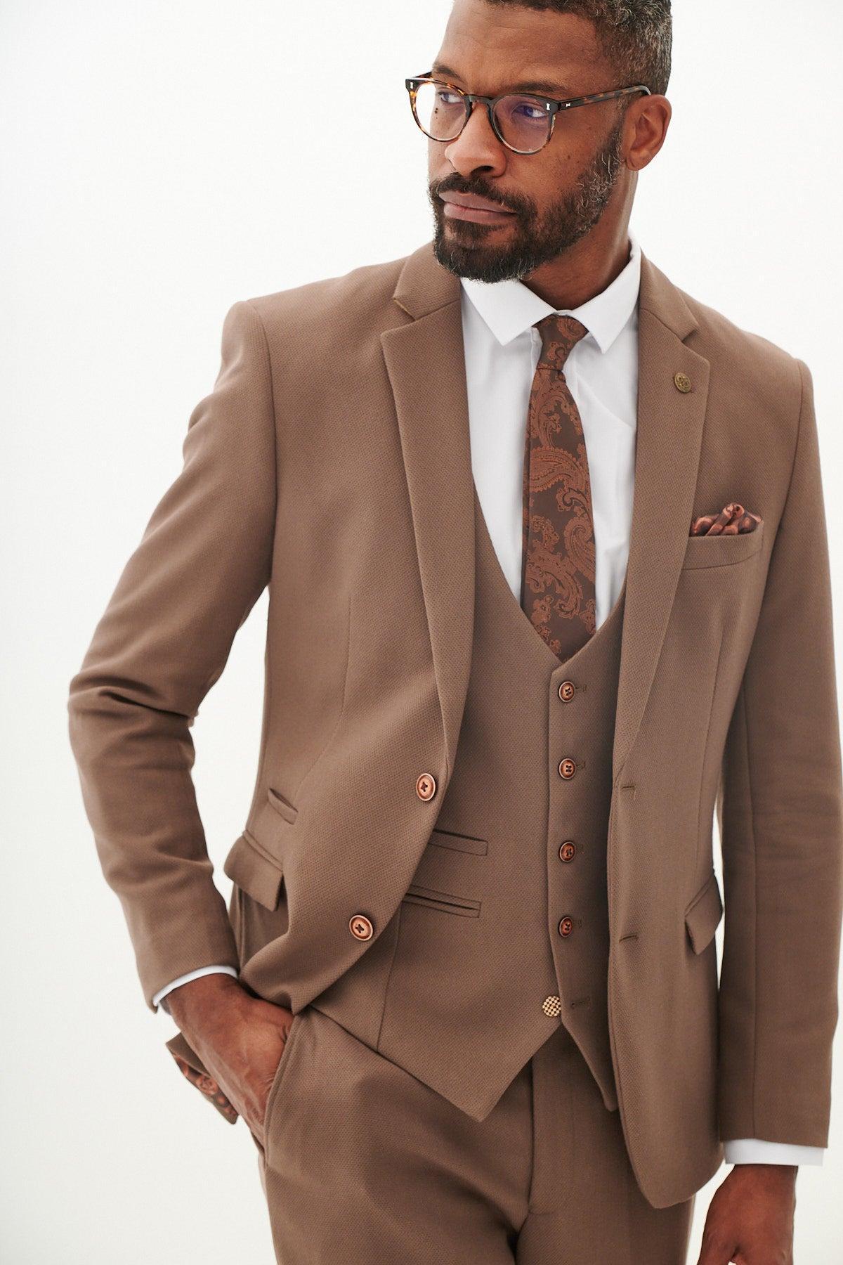 A man wears the marcdarcy HM5 - Tan Tailored Blazer with paisley lining, a white shirt, brown paisley tie, and glasses, one hand in his pocket.
