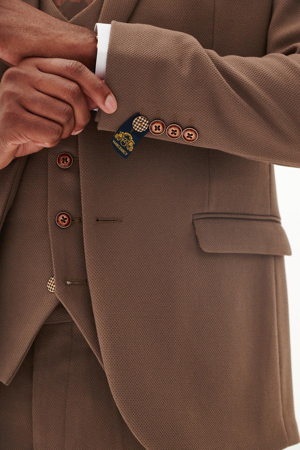 A person adjusts the cuff of a Marc Darcy HM5 - Tan Blazer with matching HM5 Stone waistcoat and trousers; only their hand and part of the torso are visible.