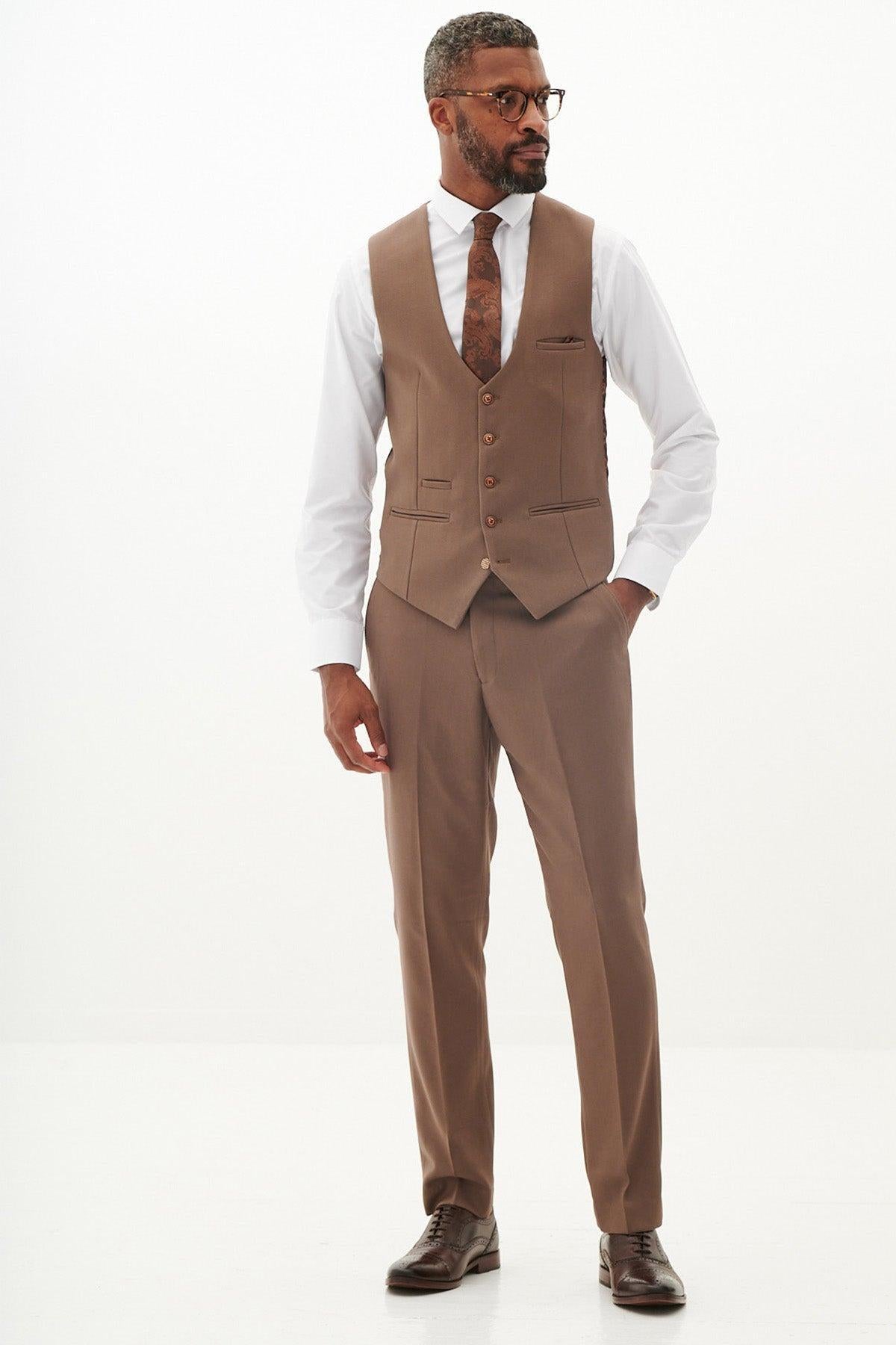 A man wearing the Marc Darcy HM5 Stone Blazer with HM5 Tan Waistcoat and Trousers (no jacket), a white dress shirt, brown tie, dark brown dress shoes, and glasses stands against a plain white background.