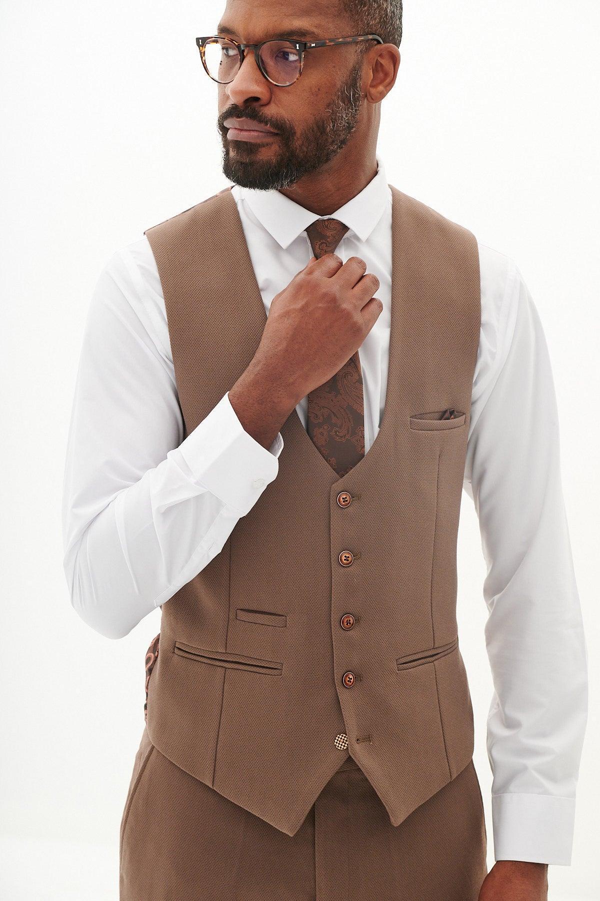 A man in glasses adjusts his brown paisley tie, wearing a white dress shirt and the marcdarcy HM5 - Tan Single Breasted Waistcoat, part of a refined three-piece suit, finished with a pocket square.