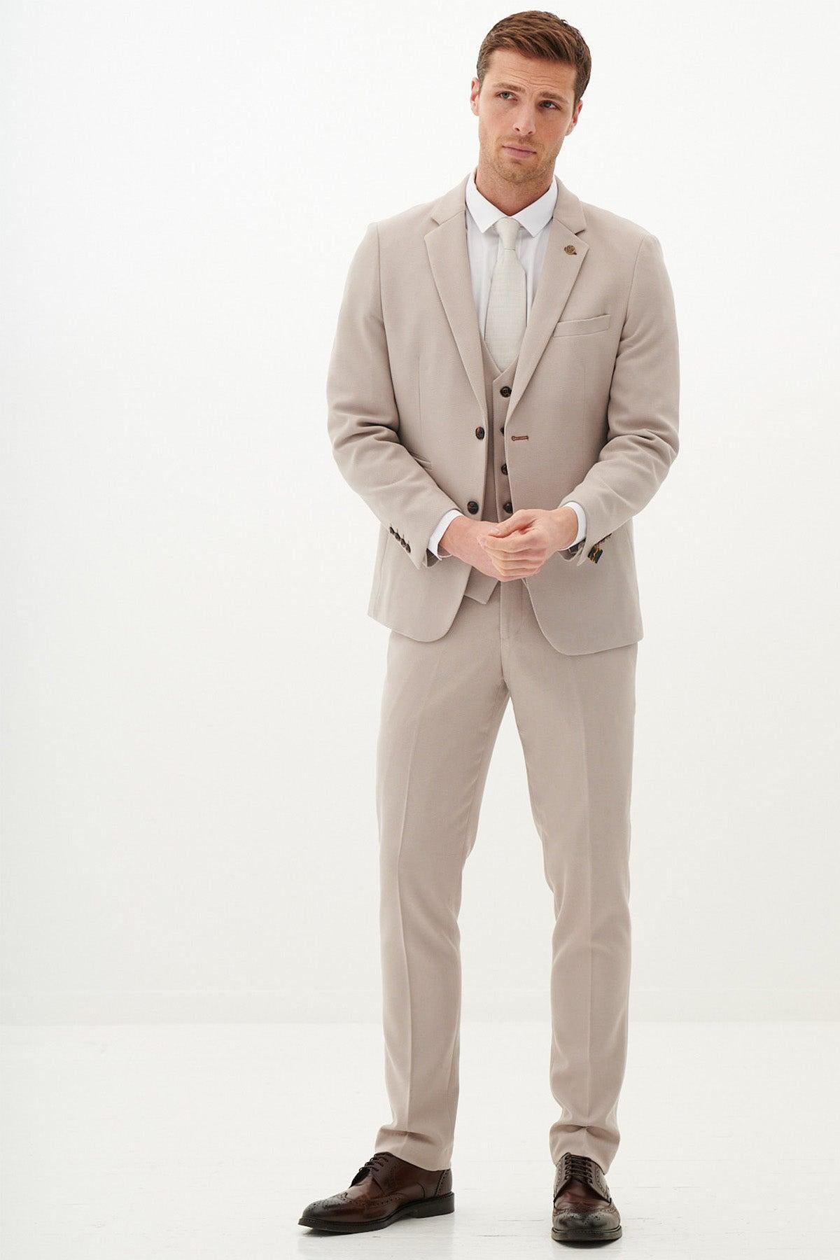 A man wears the Marc Darcy Harry Maguire Wedding Suit (HM5 Stone Three Piece Suit) with a white shirt and brown shoes, standing against a plain white background with hands relaxed by his sides, looking straight ahead.