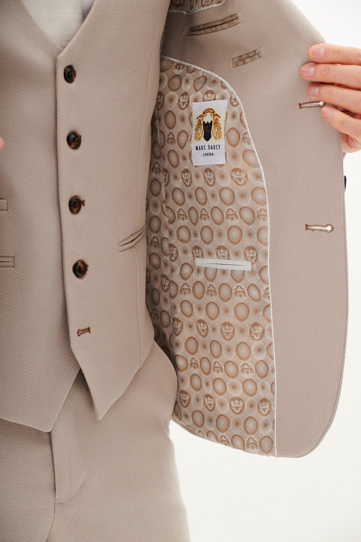 A person in a stone three-piece suit (The Harry Maguire Wedding Suit - HM5 by Marc Darcy) opens the jacket to reveal a light brown skull-patterned lining and a Marc Darcy label with lion logo—an ideal wedding suit choice.
