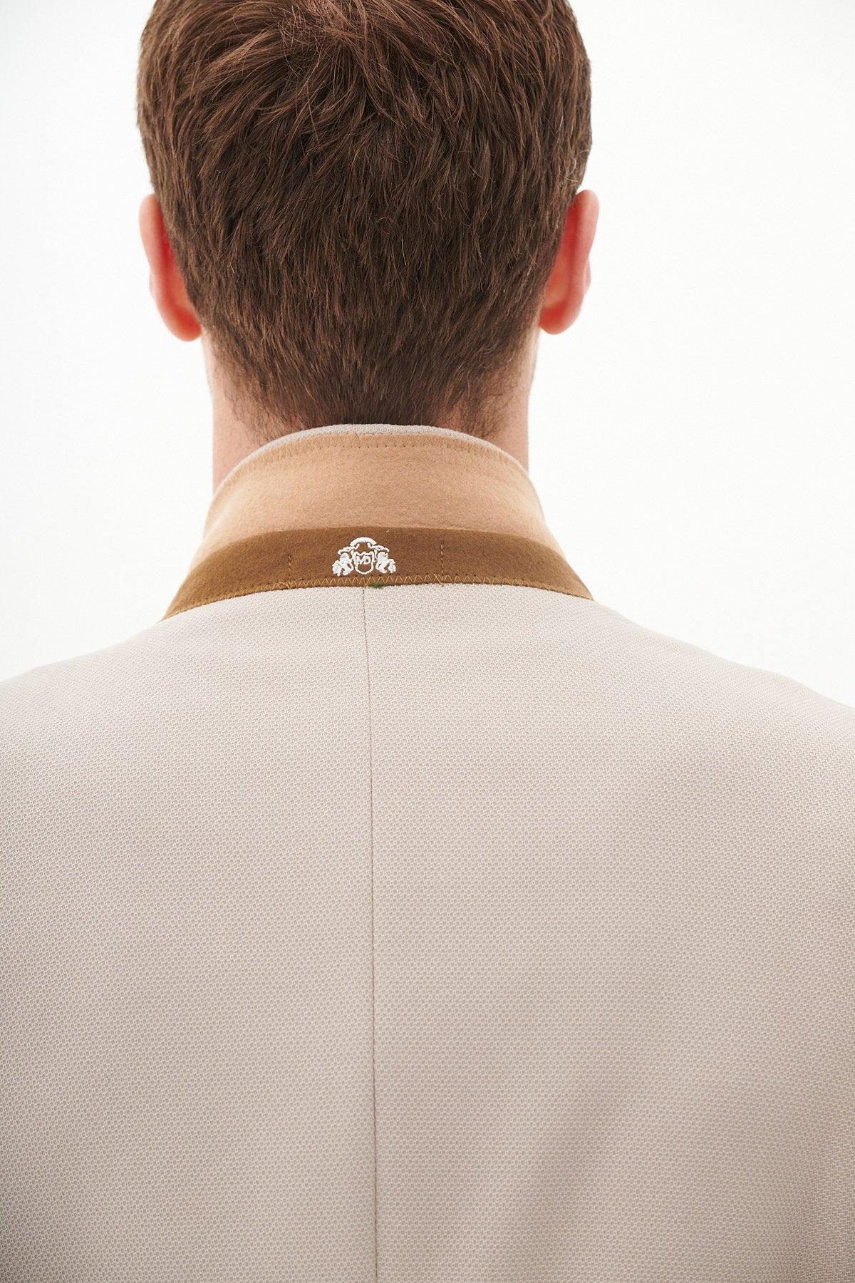 Close-up of the back of a man's head and shoulders wearing the Marc Darcy Harry Maguire Wedding Suit - HM5 Stone Three Piece Suit. The tailored blazer features a light stone hue, brown collar, and silver emblem.