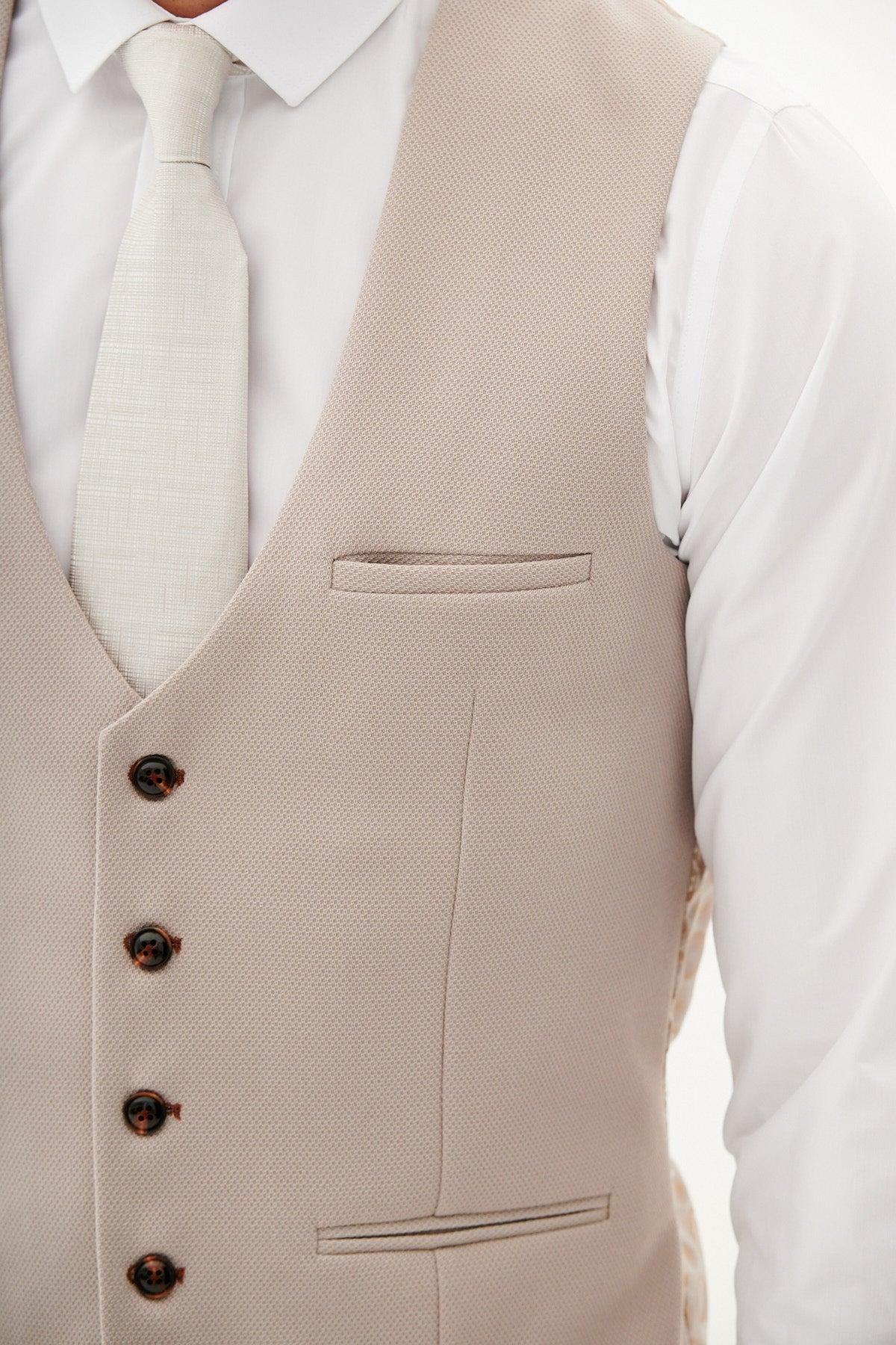 Close-up of The Harry Maguire Wedding Suit - HM5 Stone Three Piece Suit by Marc Darcy: a man wears the beige patterned vest over a white dress shirt and tie, highlighting its textured fabric, welt pocket, and dark brown buttons—perfect for weddings.