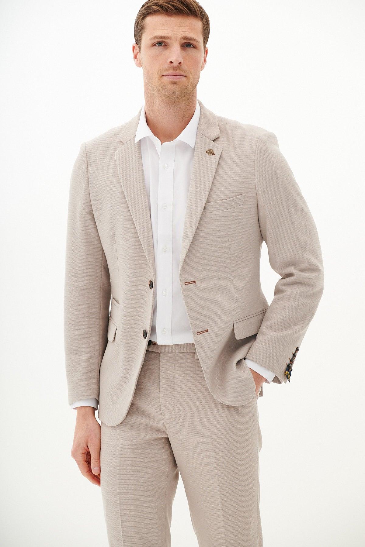 A man wears the Marc Darcy HM5 - Stone Blazer with matching tan waistcoat and trousers, styled with a white shirt. His right hand is in his pocket.