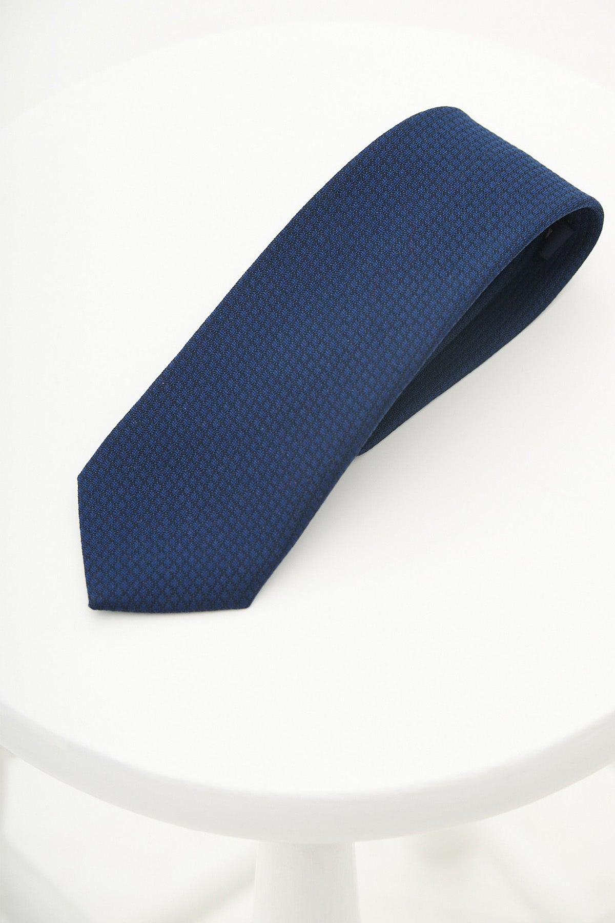 The MAX - Royal Diamond Print Tie by Accessory, featuring a navy diamond pattern and subtle texture, is elegantly displayed on a round white surface—ideal for formal wedding attire.