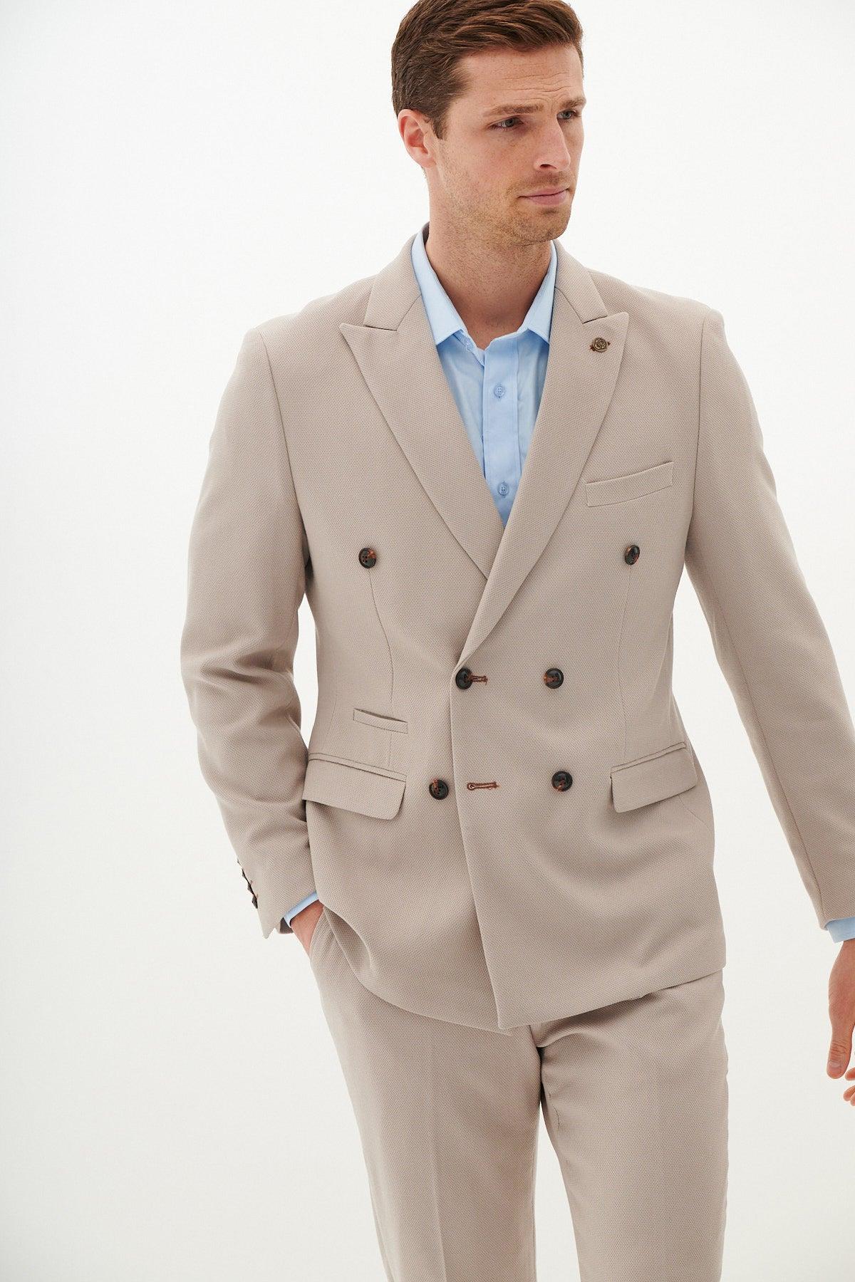 MK Dons footballer Callum Hendry wears the Marc Darcy HM5 Stone Double-Breasted Suit, styled in a slim fit with a blue dress shirt, posing against a plain white background with one hand in his pocket.