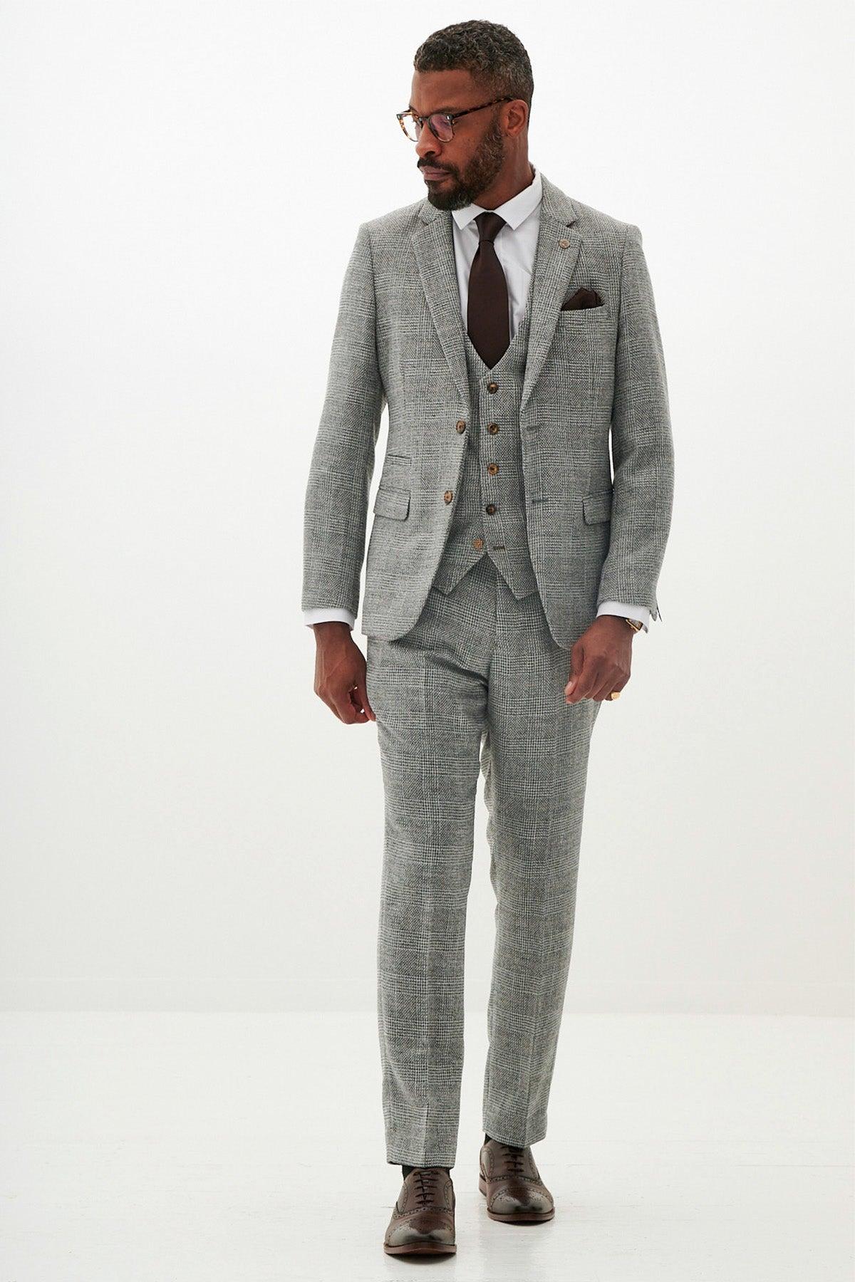 A man wears the marcdarcy KRIS Silver Grey Tweed Suit with Prince of Wales check, paired with a white shirt and dark brown tie, standing against a white background.