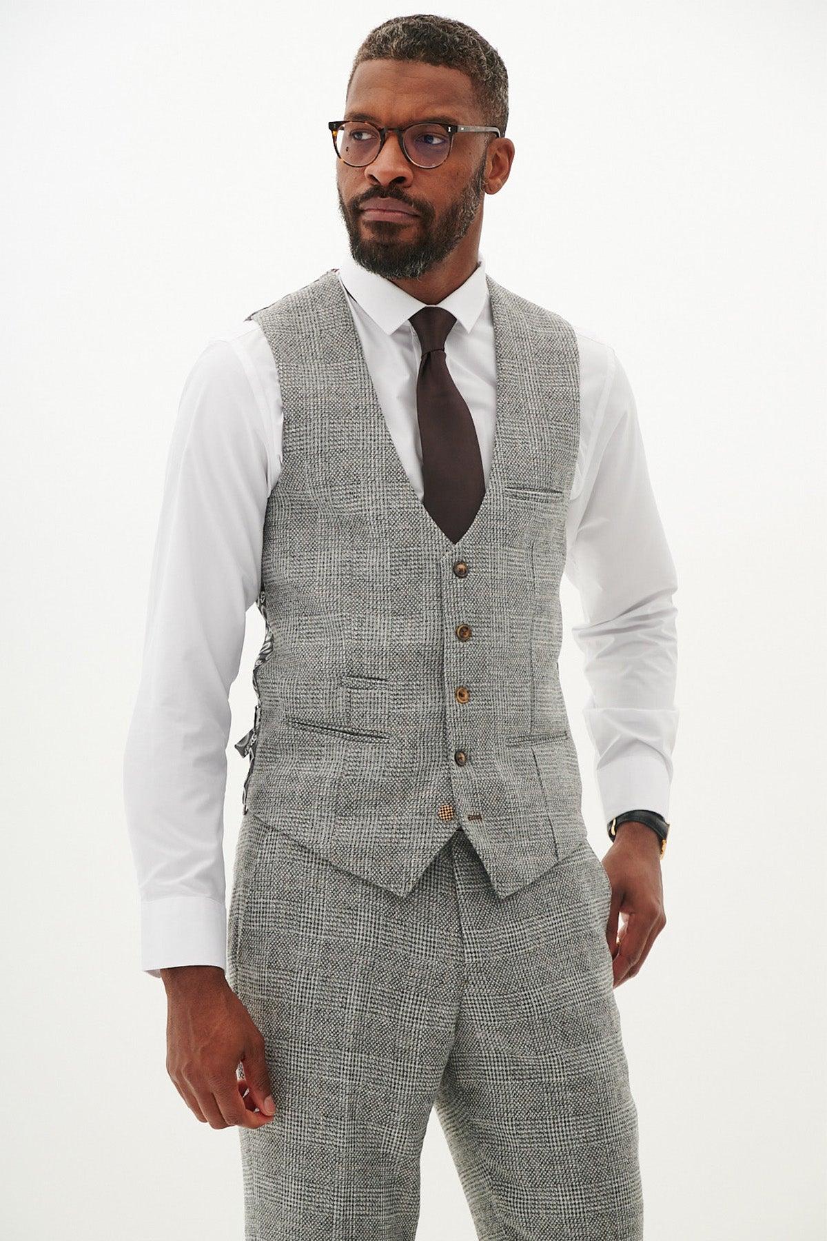 A bearded man with glasses wears the marcdarcy KRIS - Silver Grey Tweed Suit with matching trousers, a white dress shirt, and a dark tie. He stands against a plain white background, looking slightly to the side.
