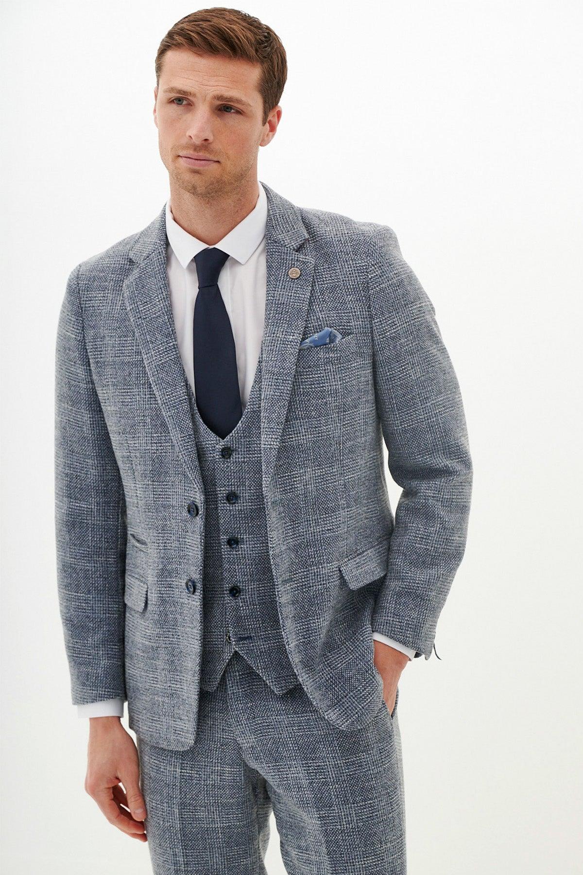Tim Iroegbunam models the marcdarcy Everton Collection KRIS Sky Blue Tweed Suit, paired with a white shirt and dark tie, standing against a plain white background with one hand in his pocket, looking slightly to the side.