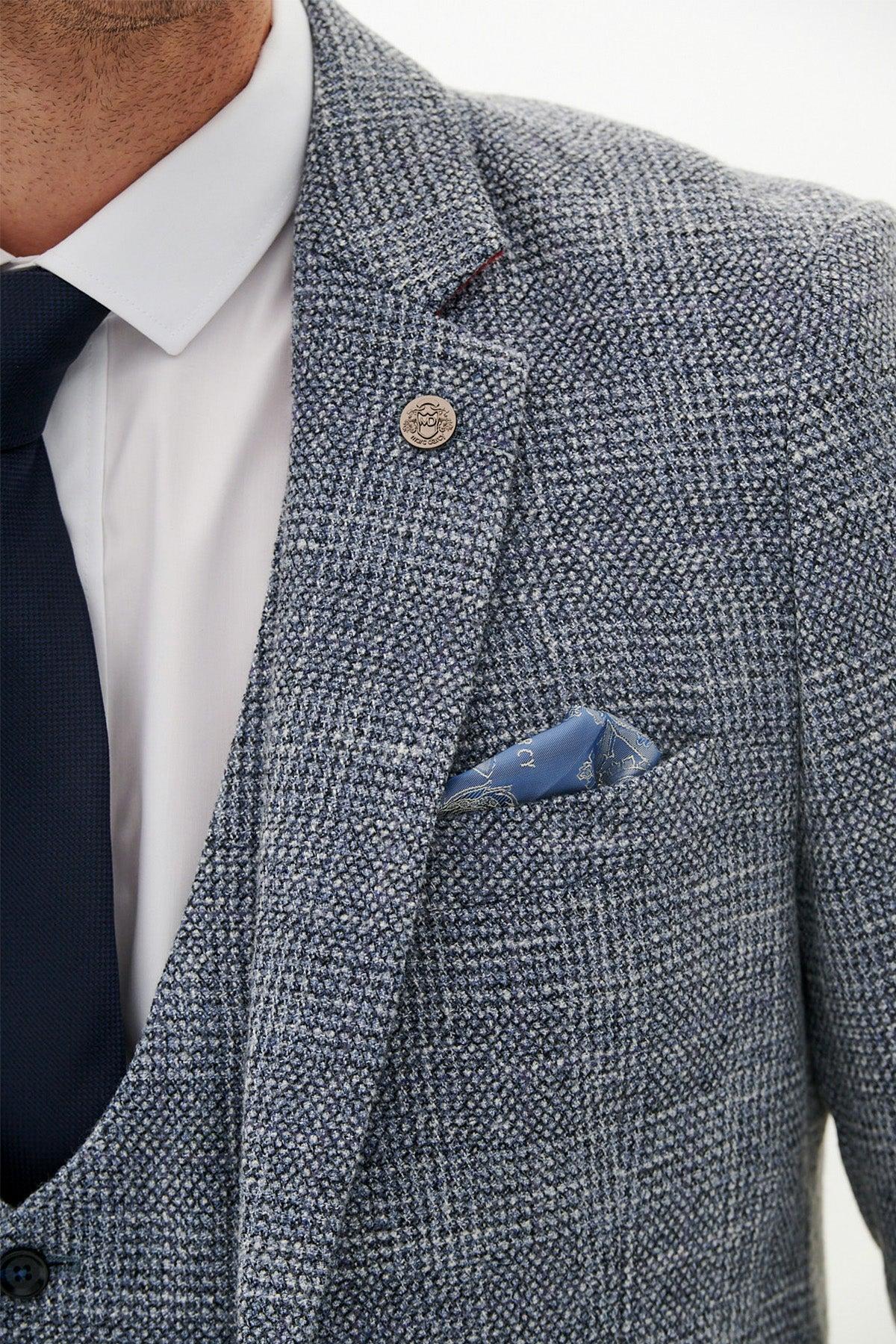 A close-up of a man wearing the marcdarcy Official West Bromwich Albion F.C. Club Suit—KRIS tweed jacket with Kelvin navy waistcoat, white shirt, dark navy tie, patterned pocket square, and silver lapel pin.