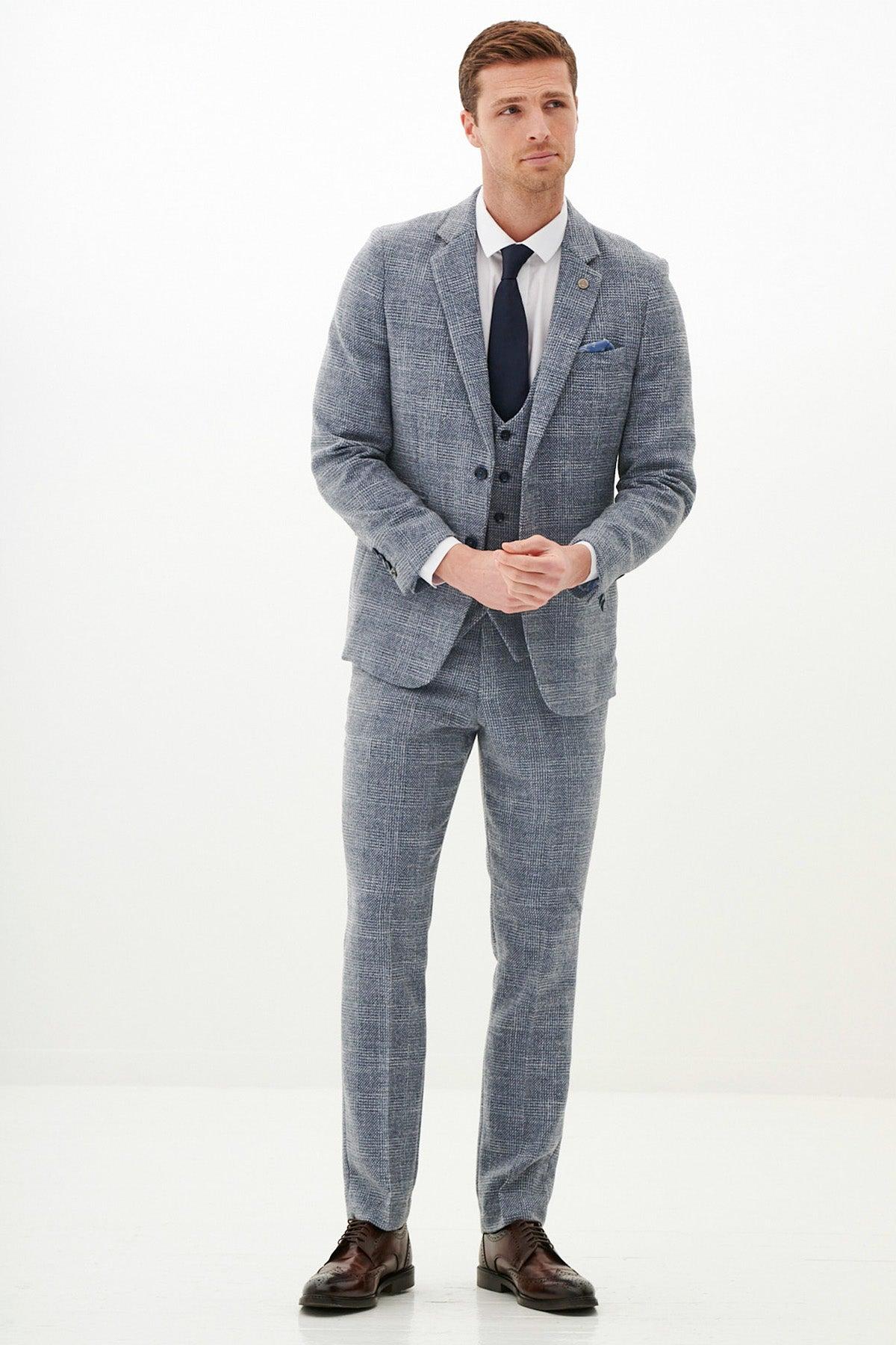 A man stands in a marcdarcy KRIS Sky Blue Tweed Suit from The Everton Collection—this slim fit ensemble, worn by Tim Iroegbunam, is paired with a white shirt and navy tie for a look of modern sophistication.