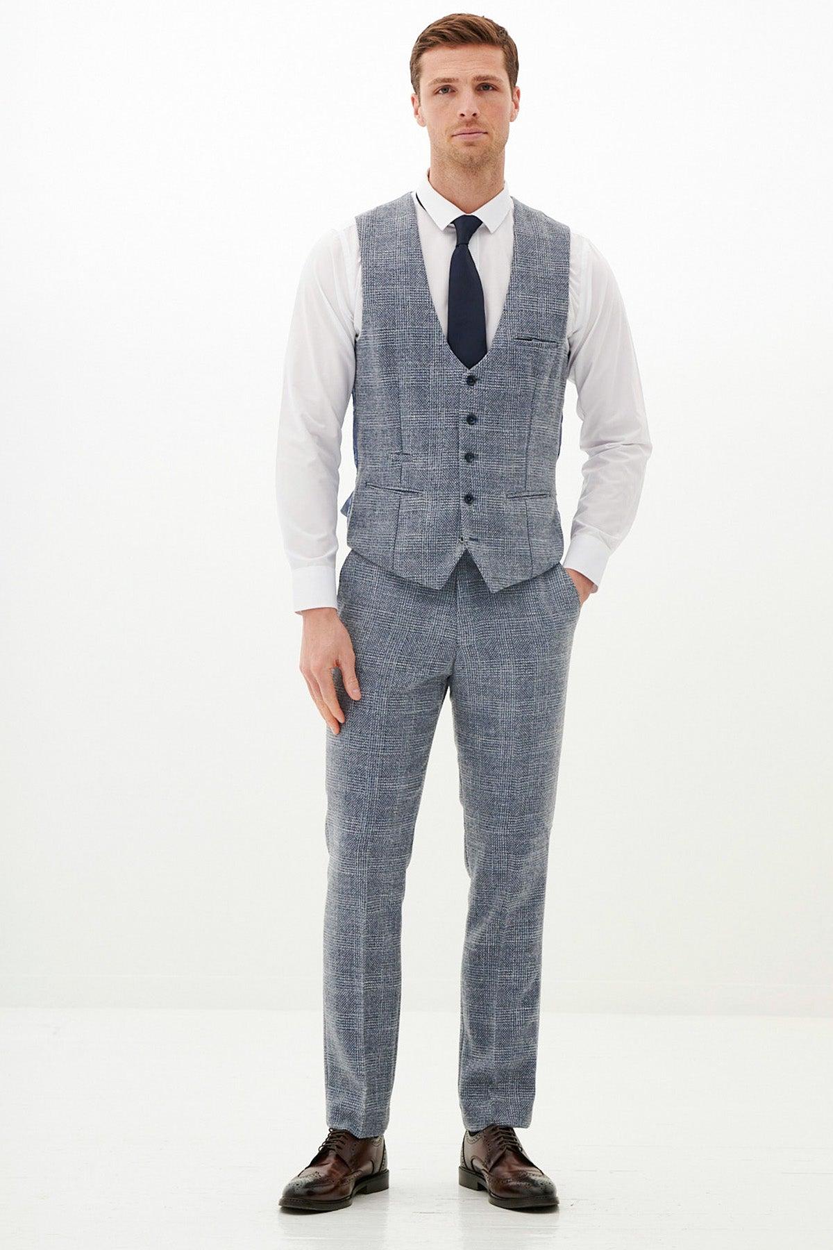 A man stands in the marcdarcy Official West Bromwich Albion F.C. Club Suit—KRIS Sky Blue Tweed Suit—with a light blue checkered vest, white shirt, matching pants, dark tie, and brown dress shoes.
