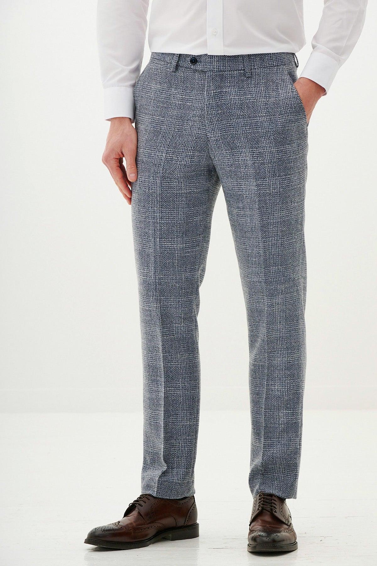 A person stands with hands in pockets against a plain white background, wearing a white dress shirt, marcdarcy KRIS sky blue tweed trousers, and brown dress shoes.
