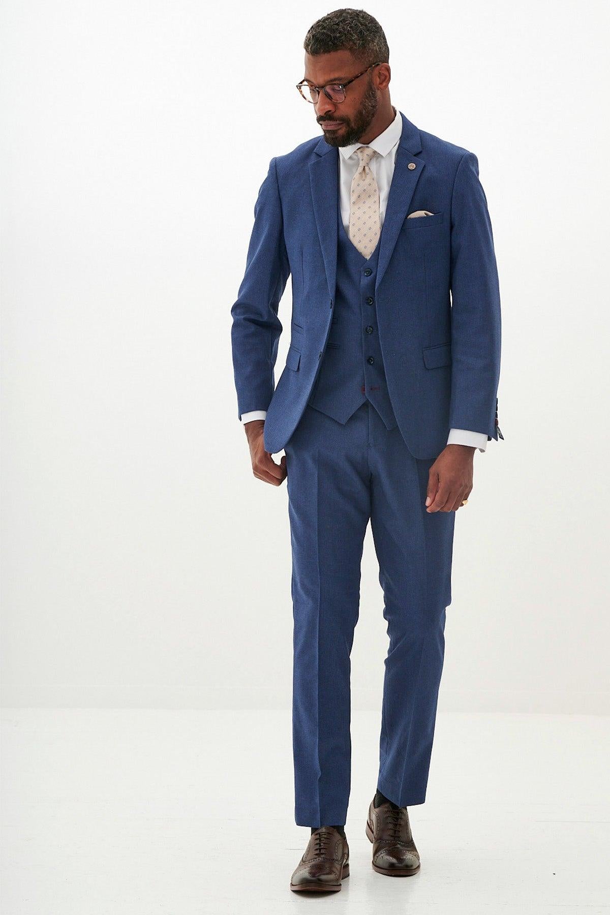 A man in the Marc Darcy Everton Collection | ASHLEY Navy Blue Three Piece Suit, white shirt, patterned tie, and brown dress shoes stands against a white background.