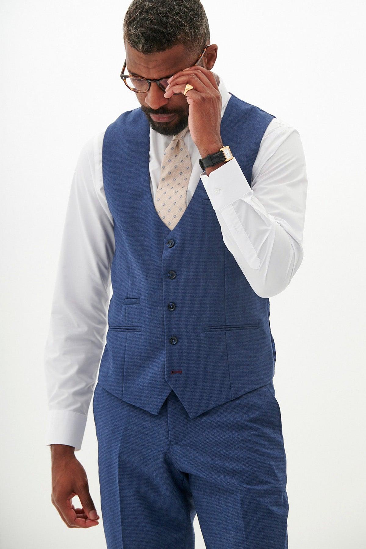 A man in the Marc Darcy ASHLEY Navy Blue Waistcoat, white shirt, and patterned tie adjusts his glasses and touches his forehead.
