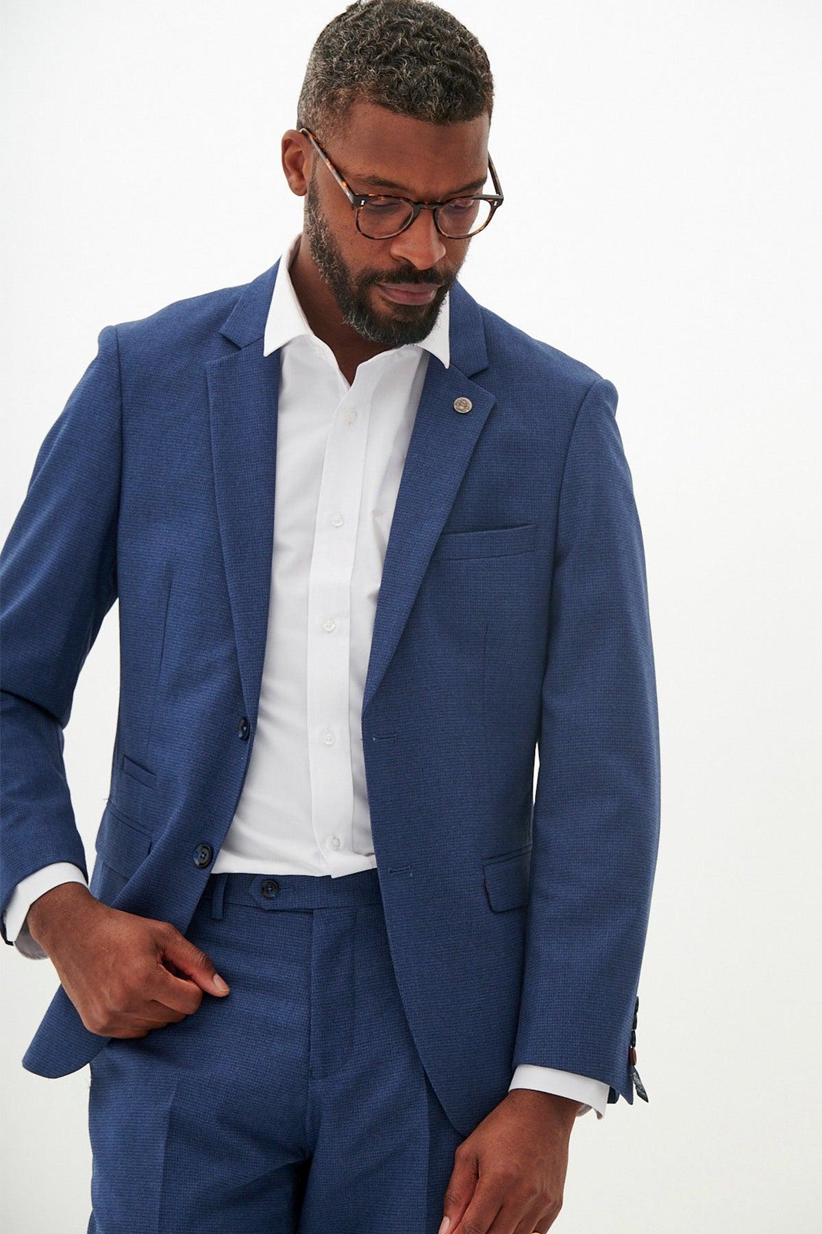 A man wearing glasses, a white dress shirt, and the Marc Darcy ASHLEY navy blue blazer adjusts his jacket against a plain white background.