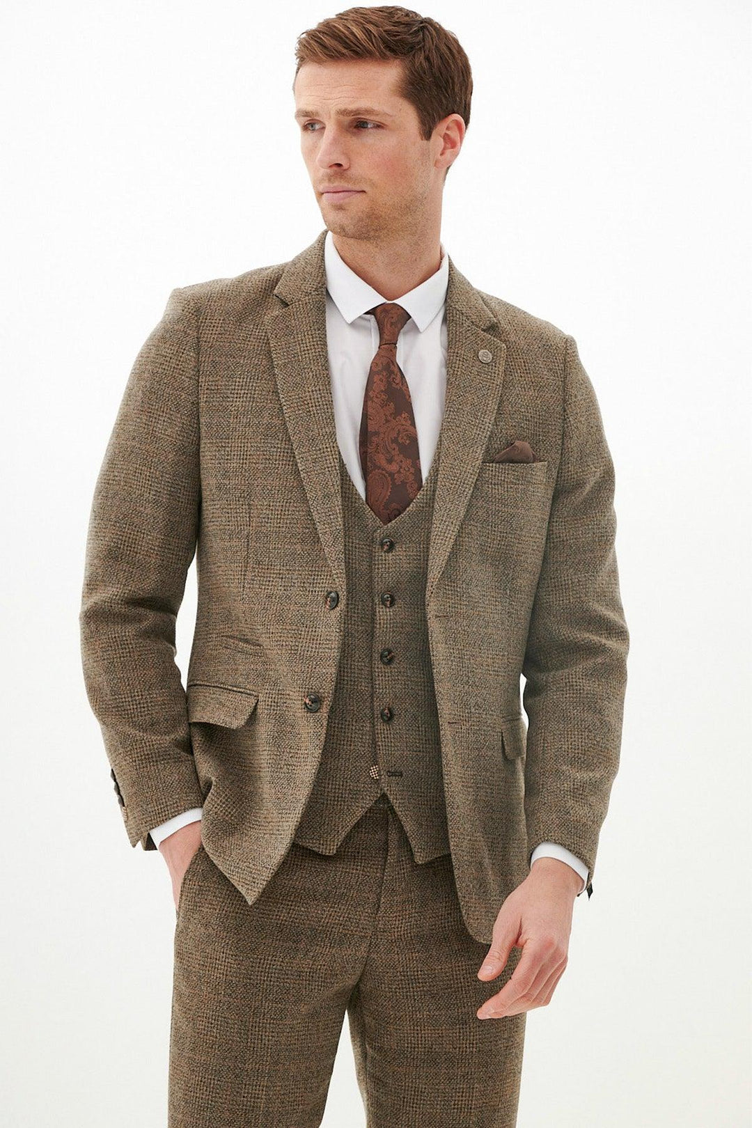 A man wearing the marcdarcy KRIS - Tan Tweed Blazer as part of a three-piece suit, paired with a white dress shirt, patterned brown tie, and matching pocket square, stands against a white background looking to his left.
