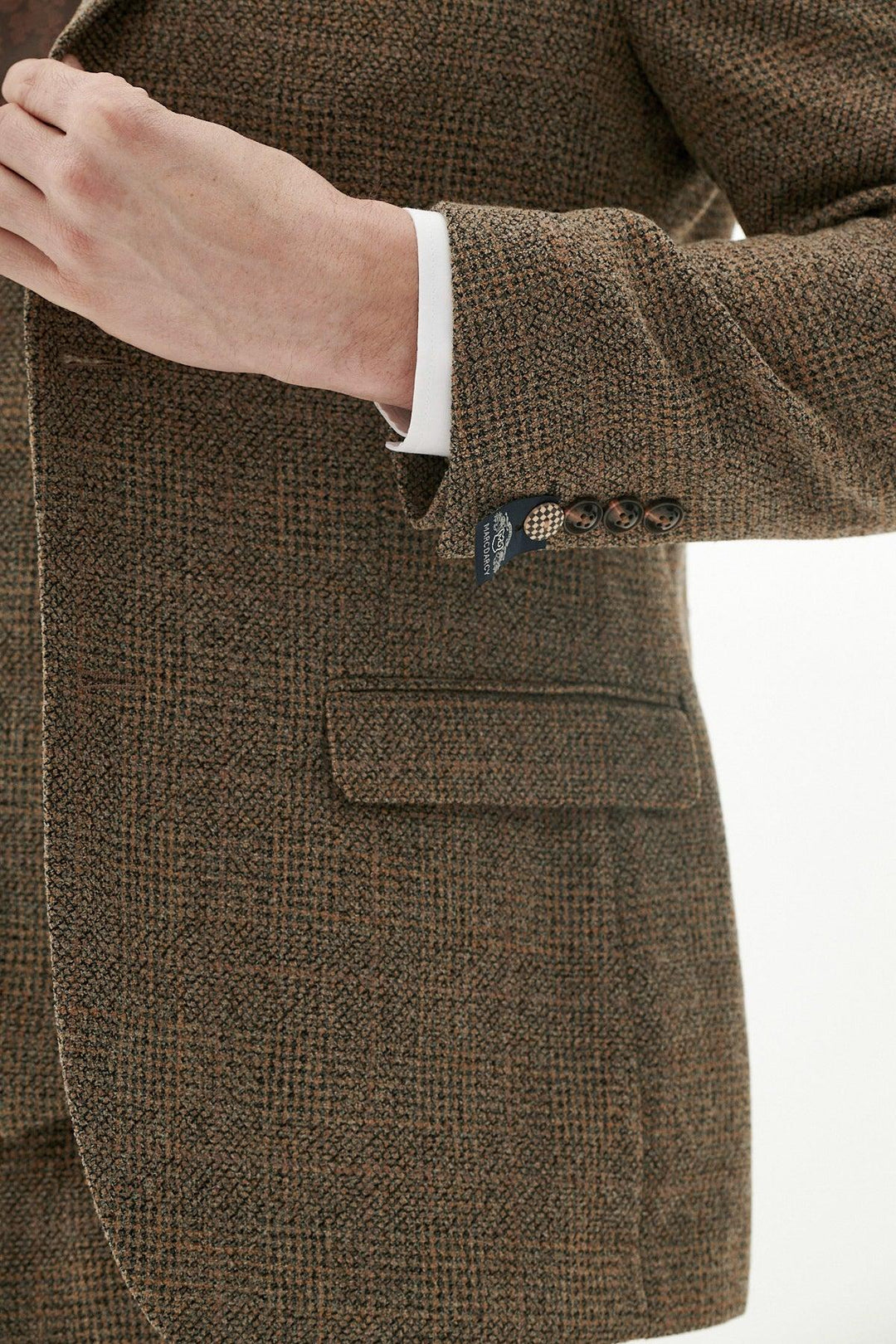 A close-up of someone adjusting the marcdarcy KRIS Tan Tweed Three Piece Suit, featuring white shirt cuffs, dark brown sleeve buttons, and a flap pocket on the jacket, set against a plain background.